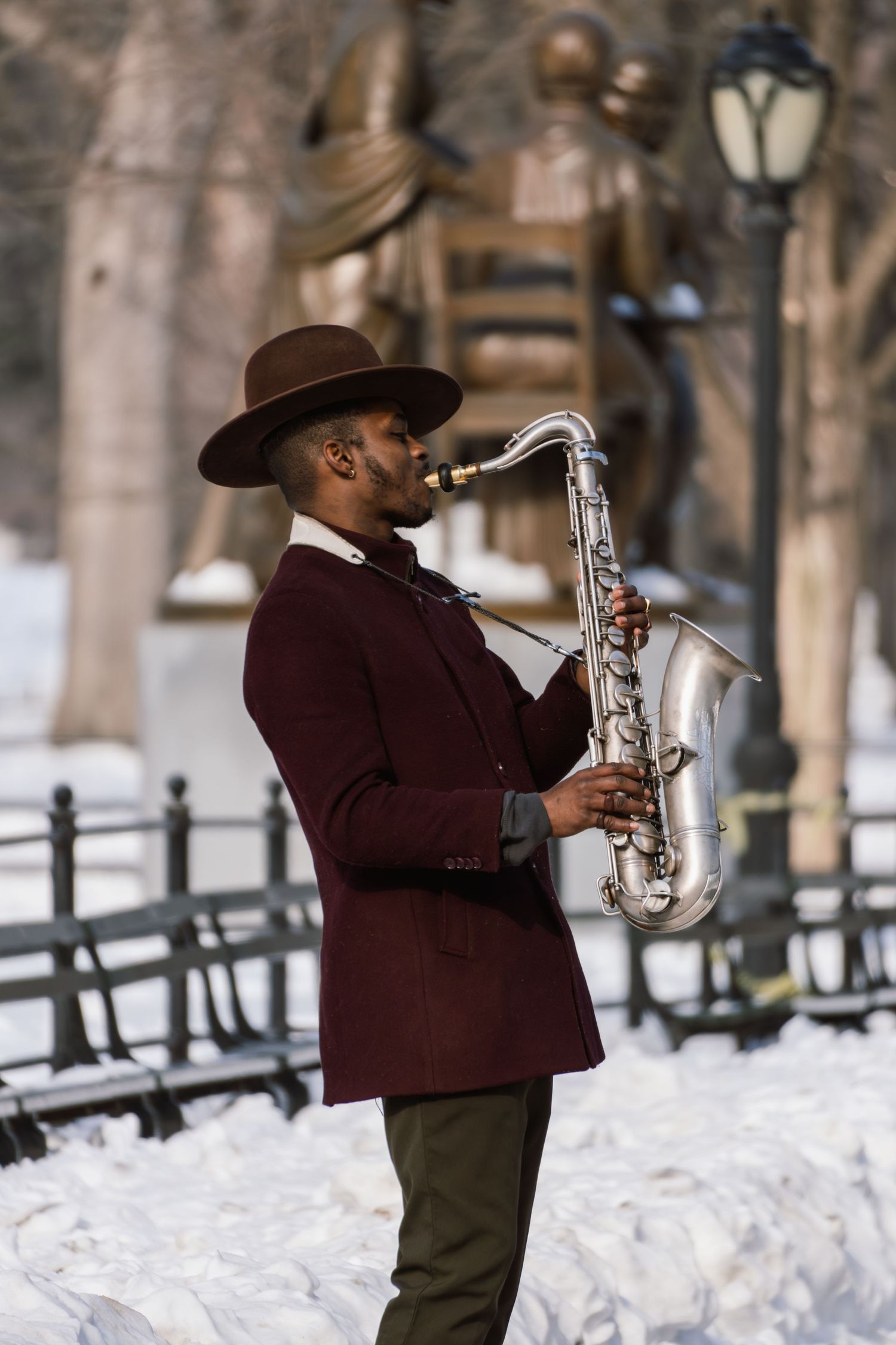 An elegant street musician plays tenor saxophone in Central Park during winter with snow on the ground.