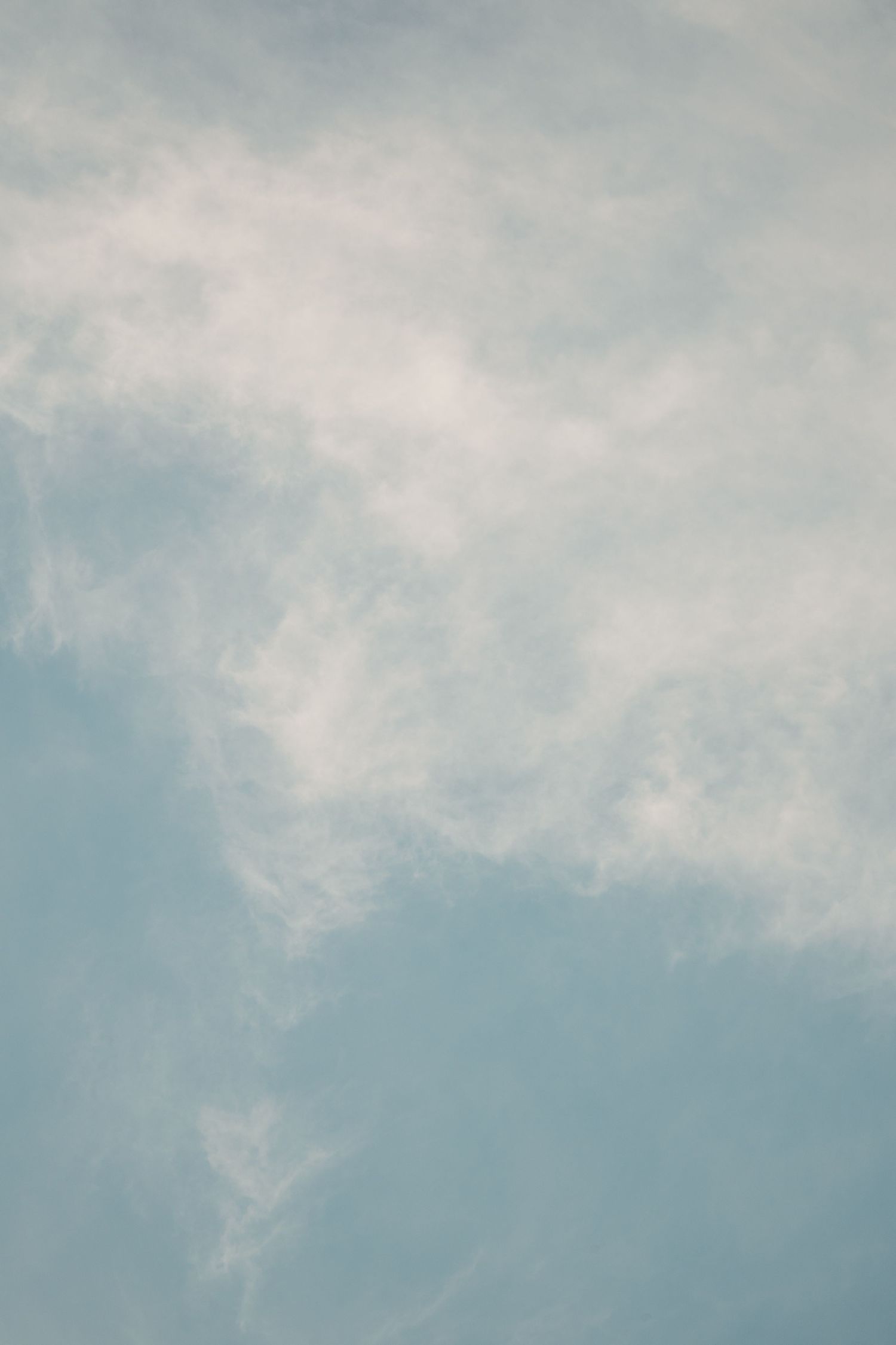 Soft white clouds drift across a pale blue sky in a serene nature photograph.