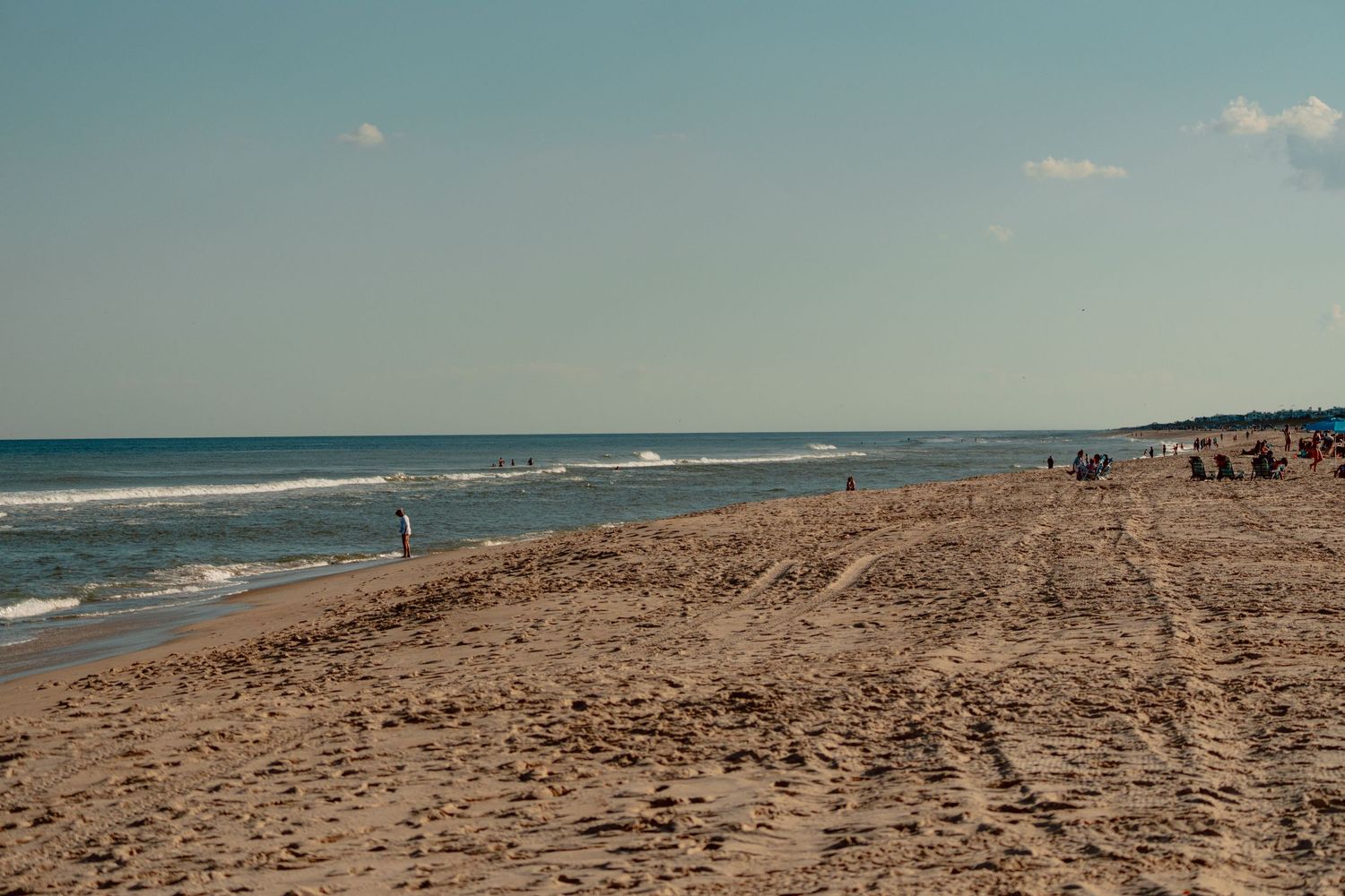 A wide sandy beach stretches along the Atlantic Ocean shoreline with gentle waves and beachgoers visible in the distance.