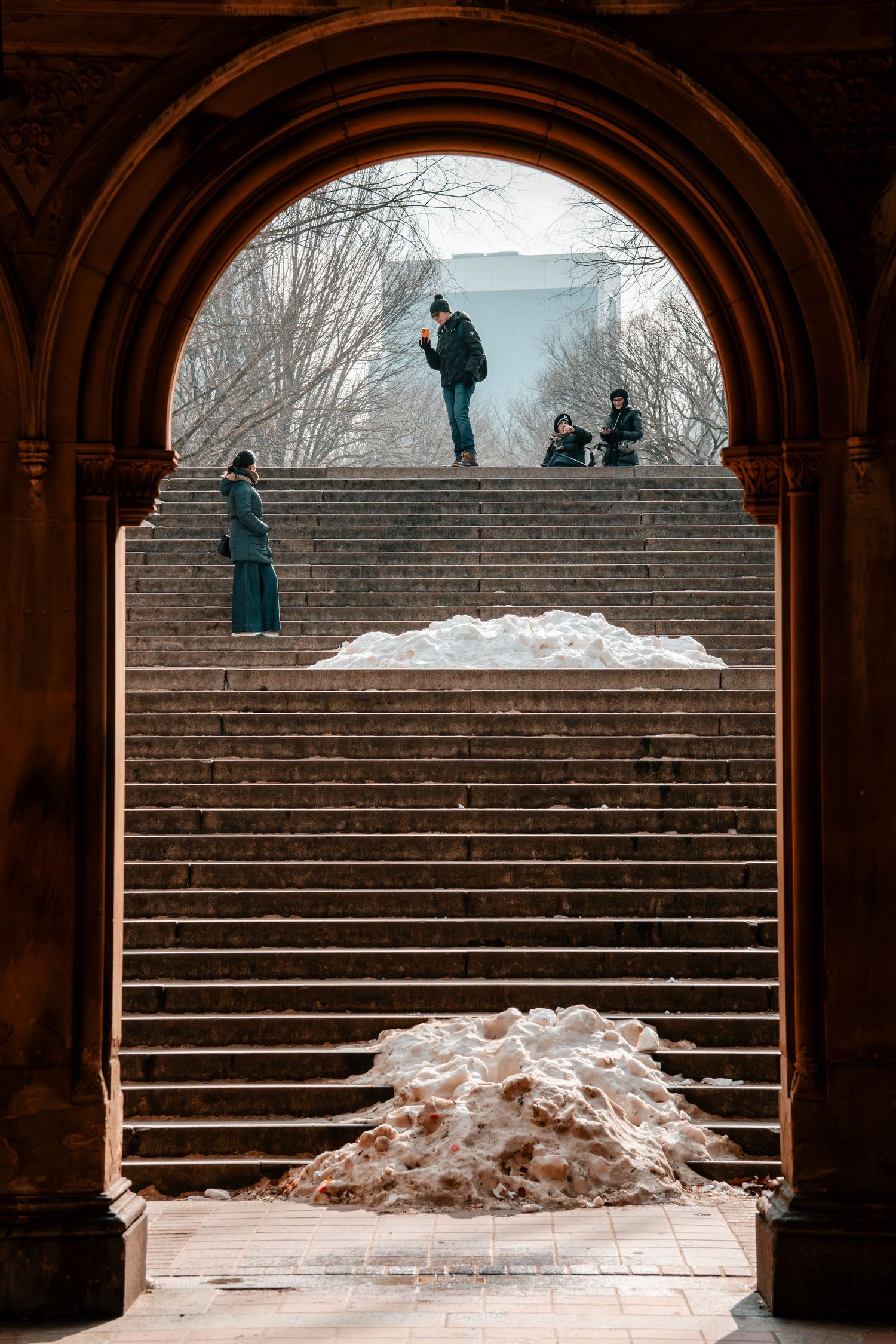 Snow-covered steps at Bethesda Terrace viewed through stone arch in Central Park during winter.