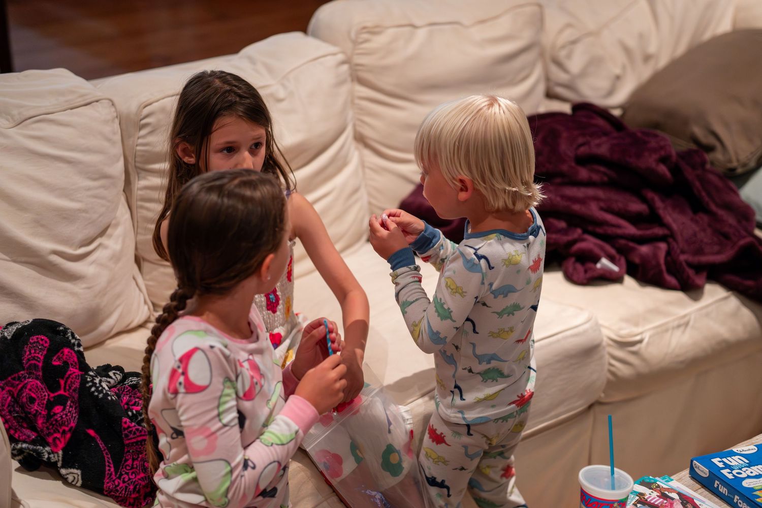 Three young children in pajamas interacting together on a white couch.