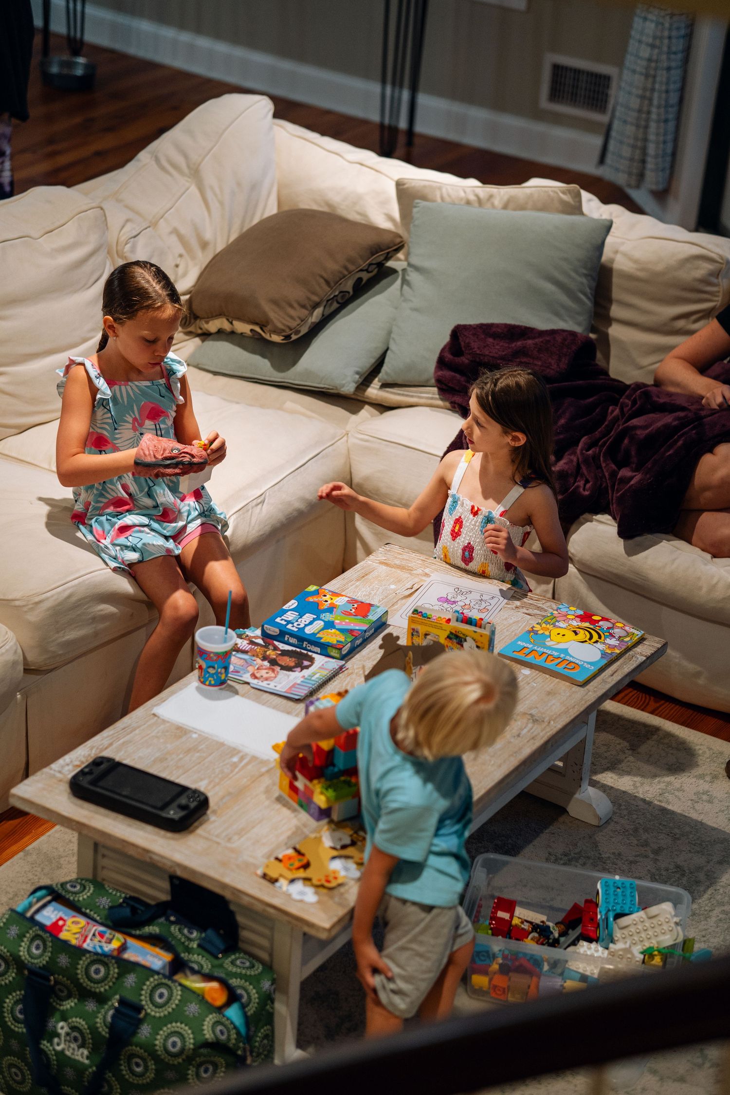 Three children playing with toys and games on a coffee table in a cozy living room.