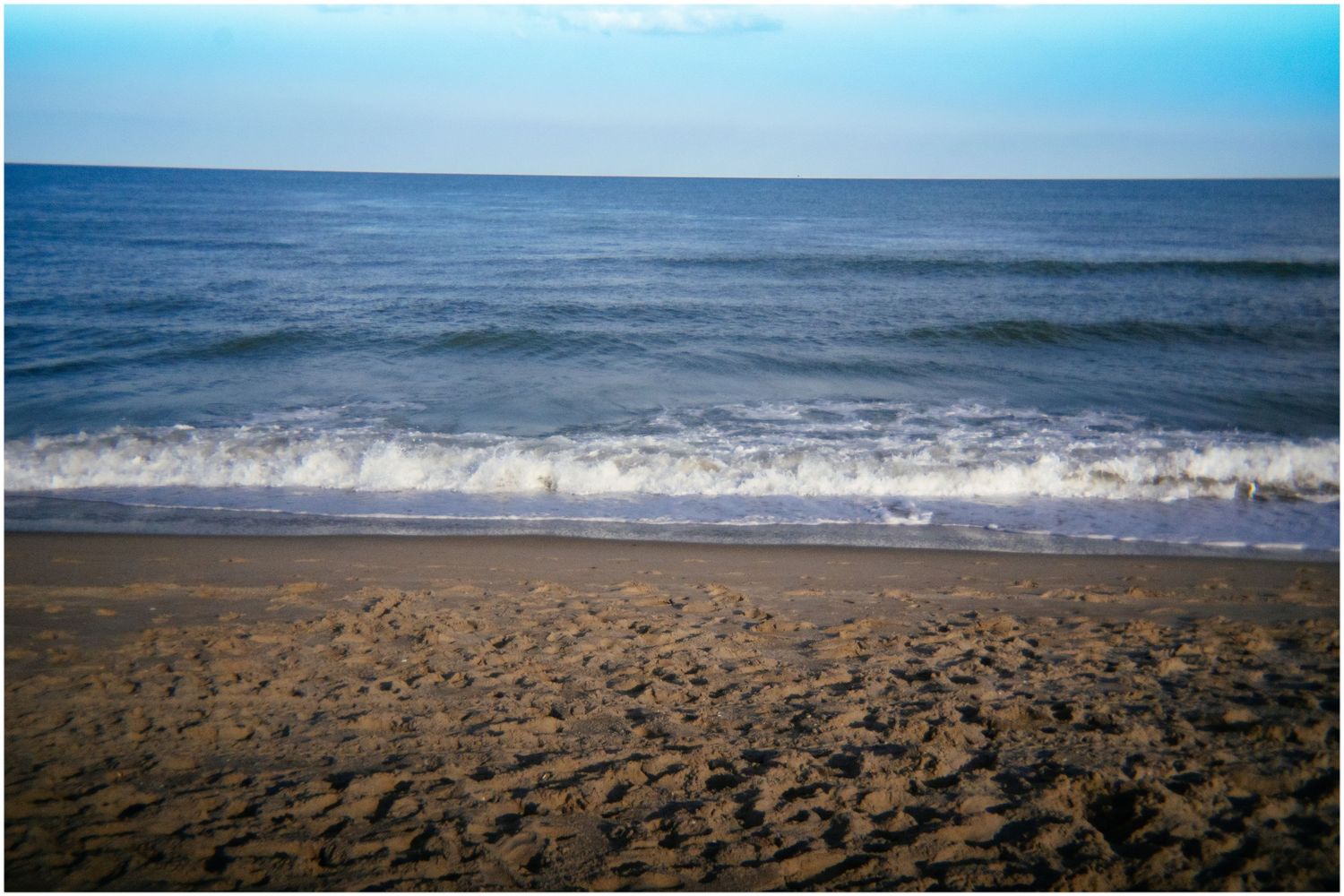 Gentle ocean waves washing onto a sandy beach under a calm blue sky.