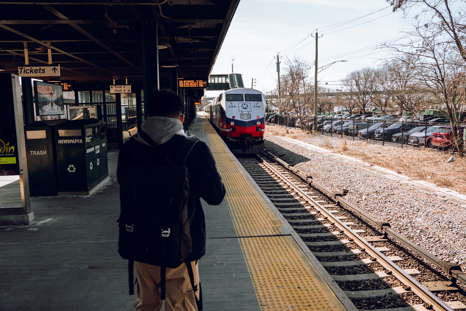 Person photographing an approaching Amtrak train arriving at a suburban commuter rail station platform.