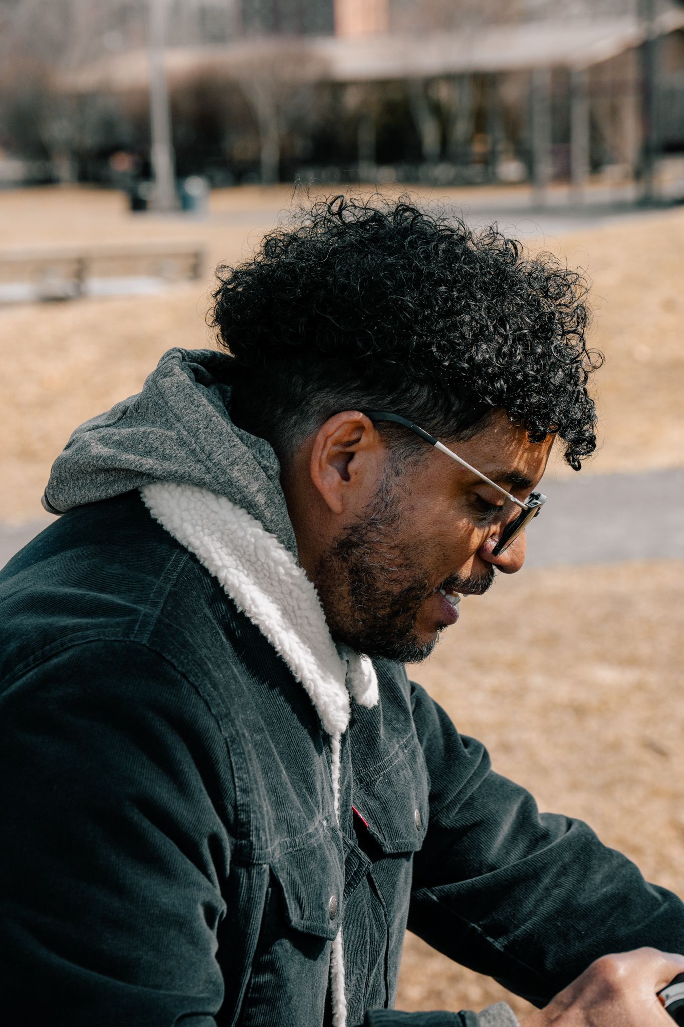 Close-up side portrait of Black man with curly hair and glasses in park.