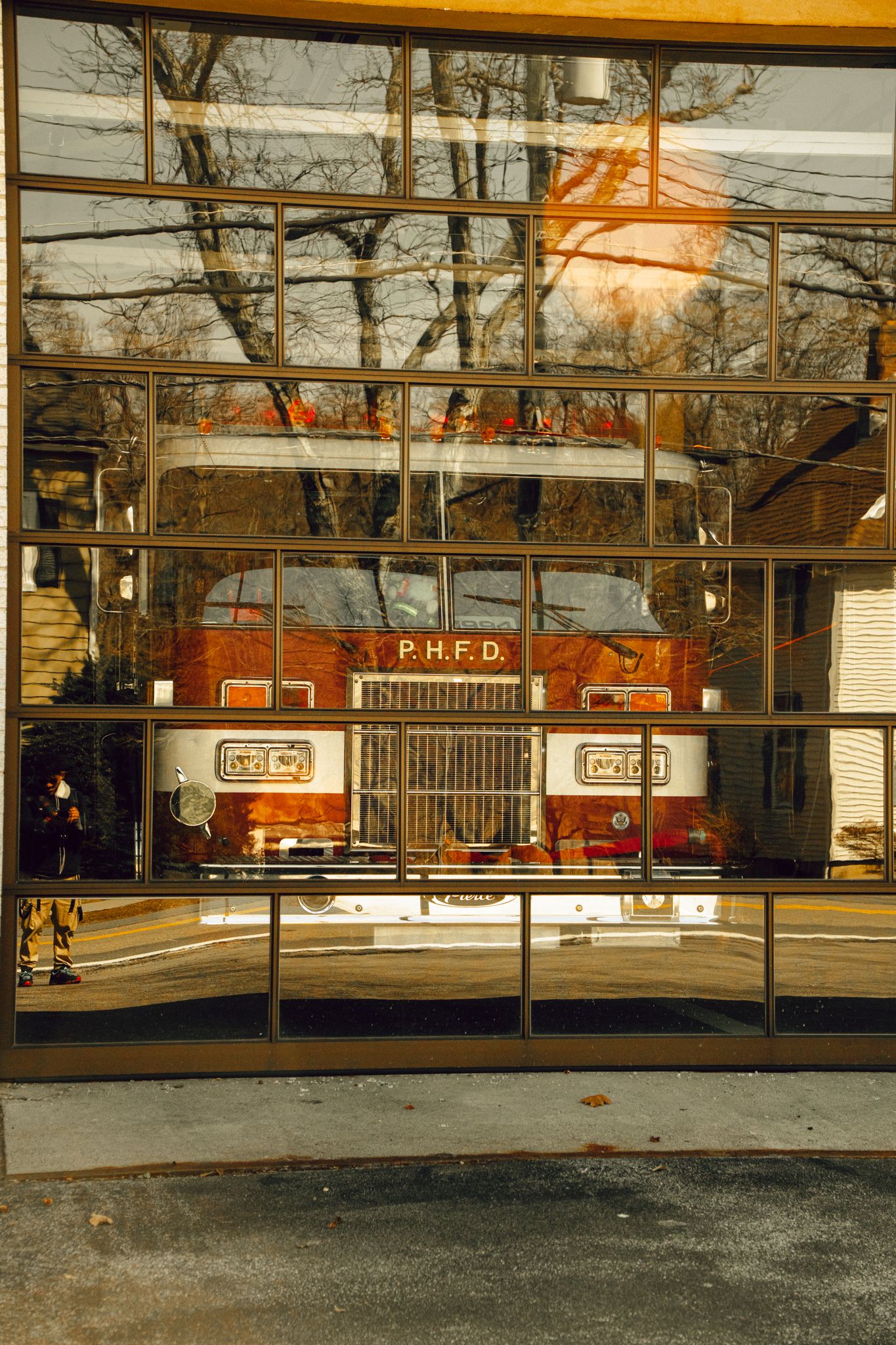 P.H.F.D. fire truck reflected in large glass garage doors of a firehouse with tree reflections.