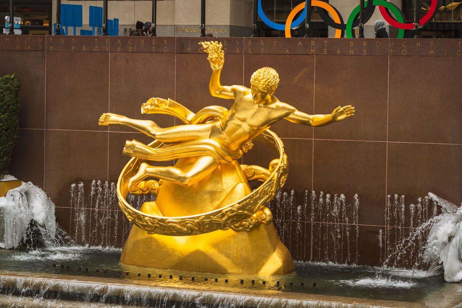 Golden Prometheus statue fountain at Rockefeller Center NYC with Olympic rings in background.