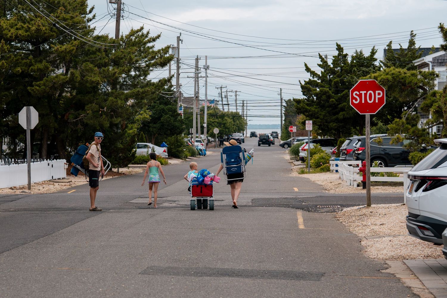 Family walking down a residential street toward the beach past a stop sign on a sunny summer day.