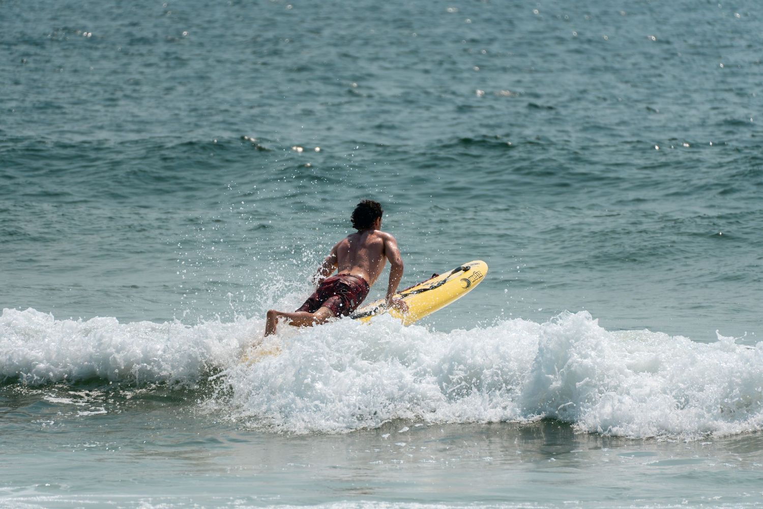 A surfer rides a yellow board through ocean waves on a sunny beach day.