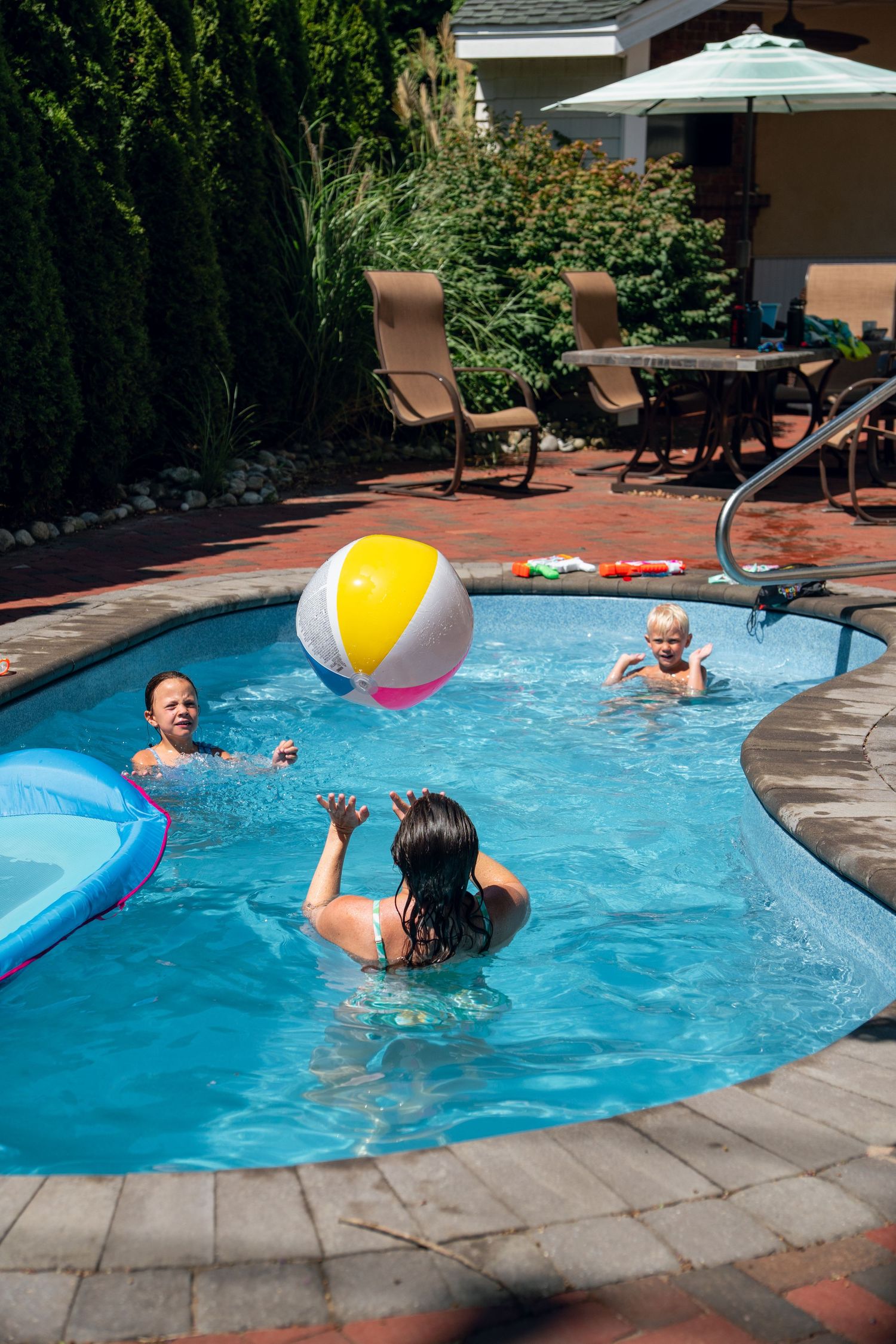 Family enjoying a sunny day playing with a beach ball in a private backyard swimming pool.