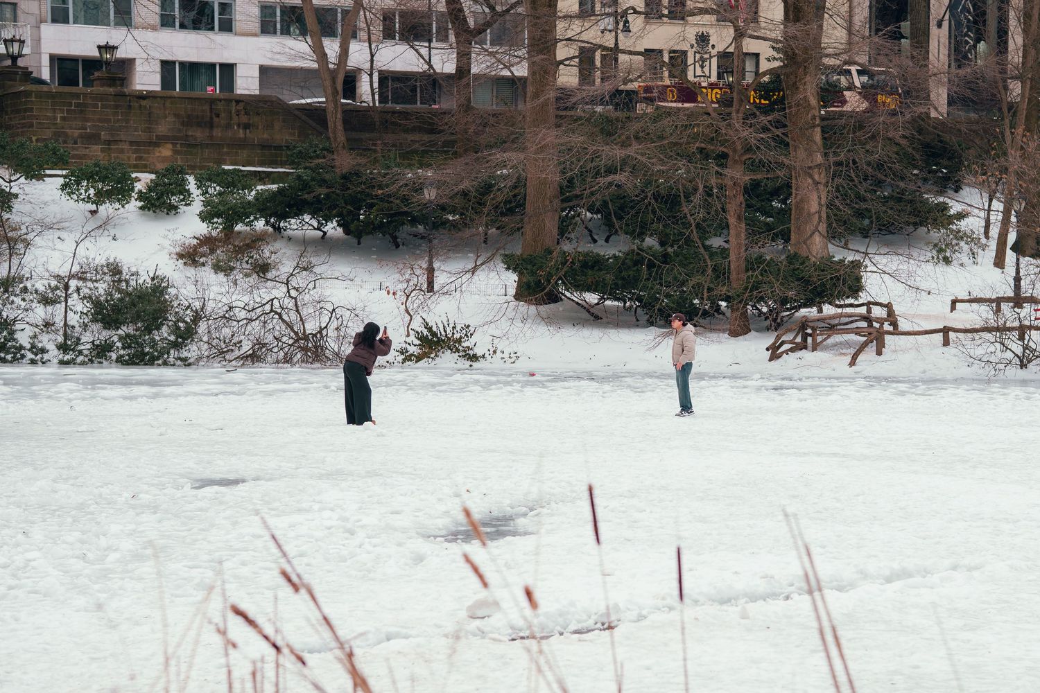 Two people standing on a frozen snowy pond in an urban park during winter.