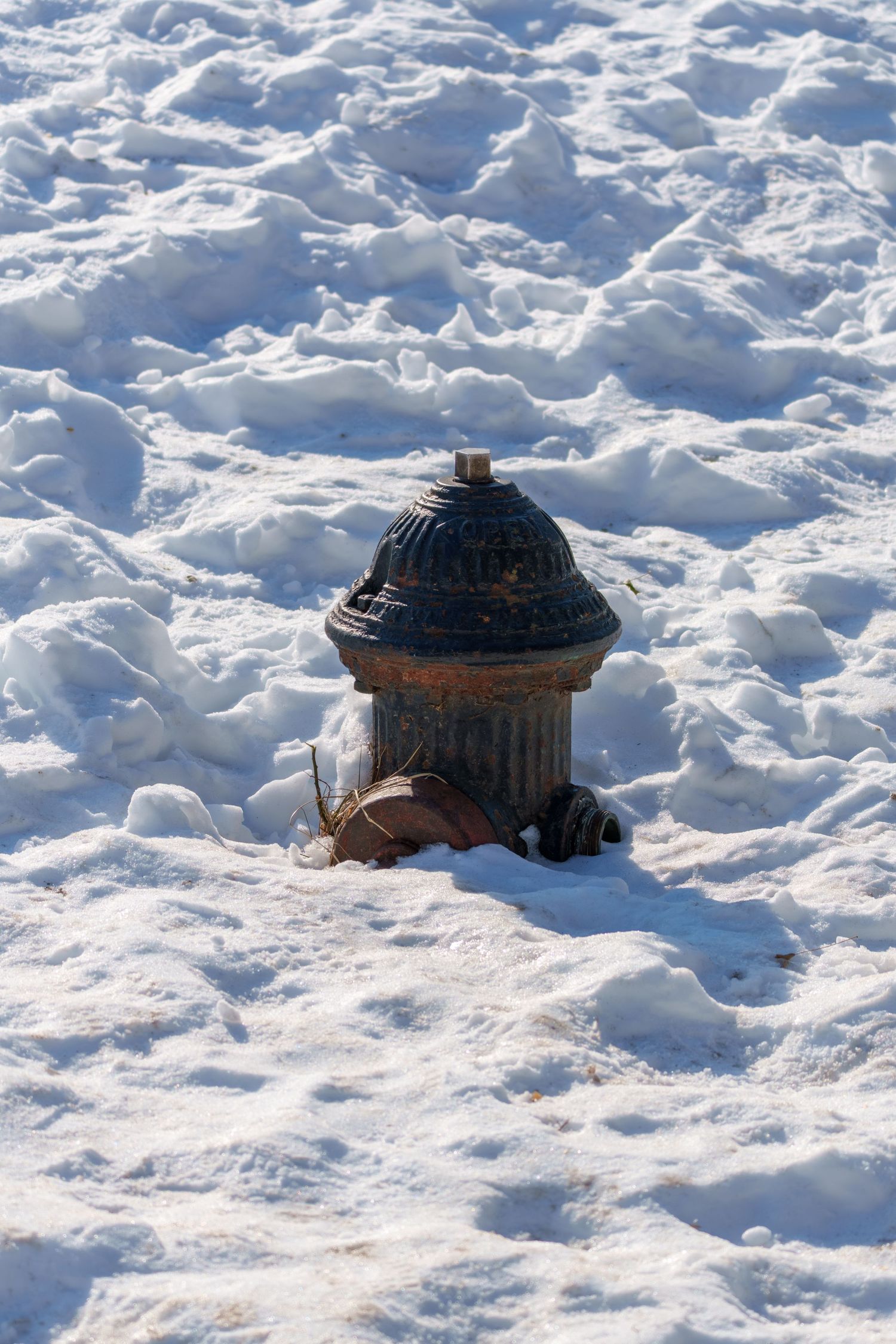 A rusty vintage fire hydrant buried in deep white snow on a bright sunny winter day.