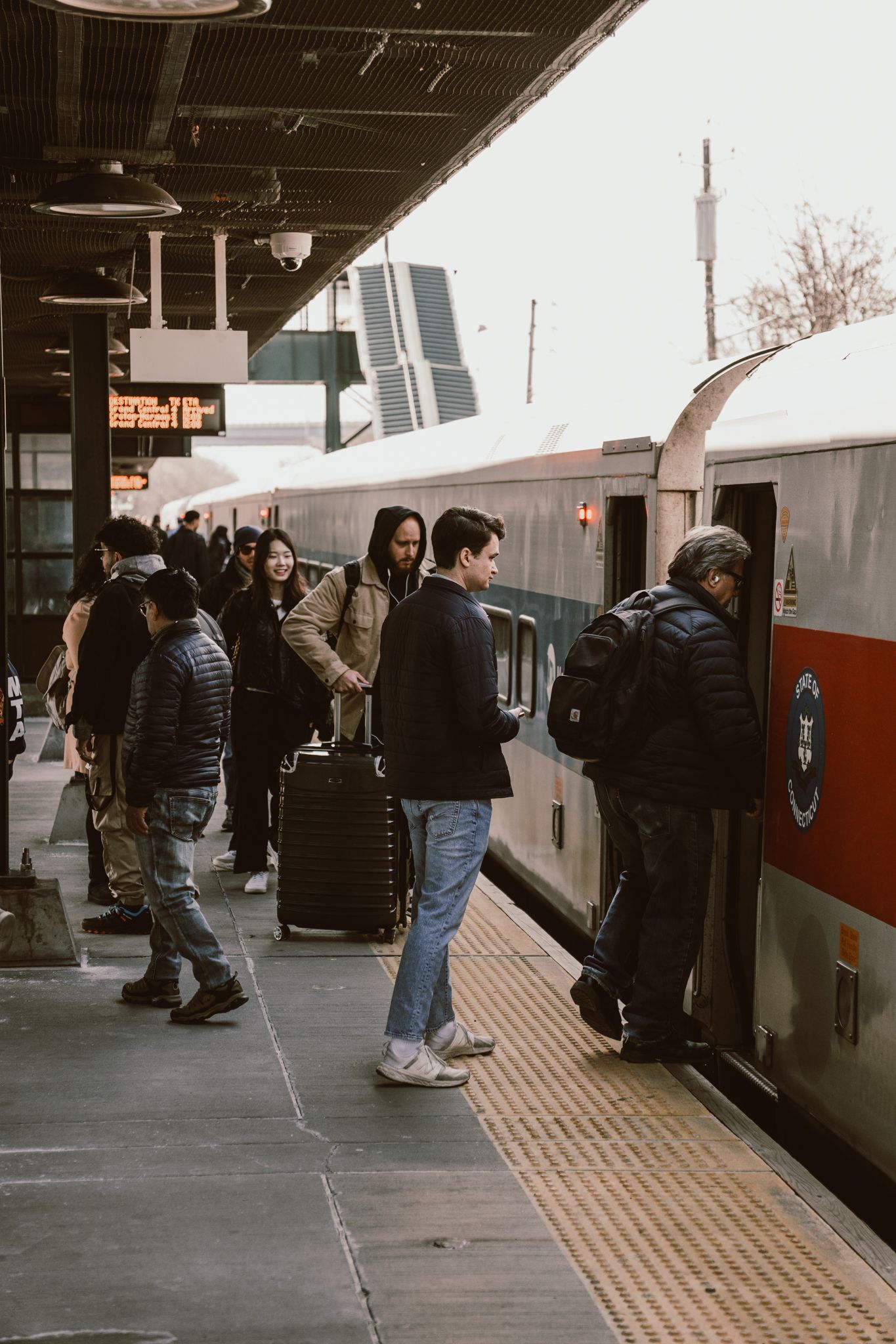Commuters boarding a Metro-North passenger train at a busy station platform with luggage and backpacks.