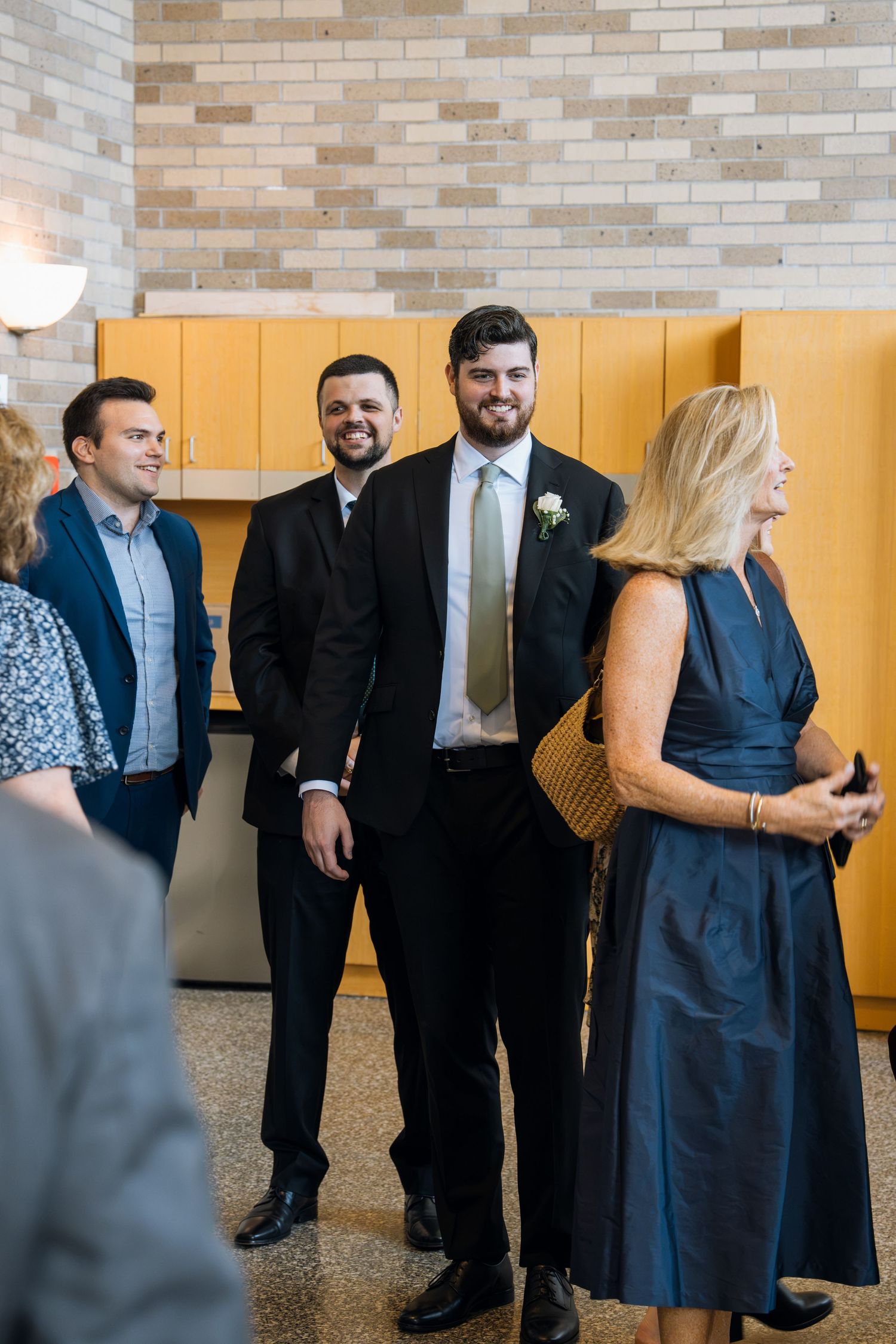 Groom in black suit with white boutonniere smiles with groomsmen at wedding reception venue.