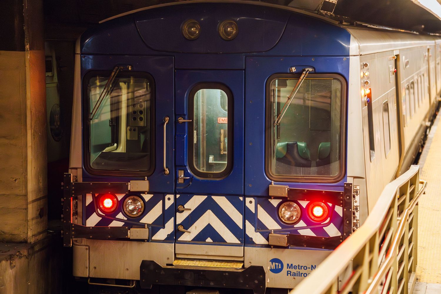 A blue Metro-North Railroad commuter train with chevron markings sits at a dark station platform.