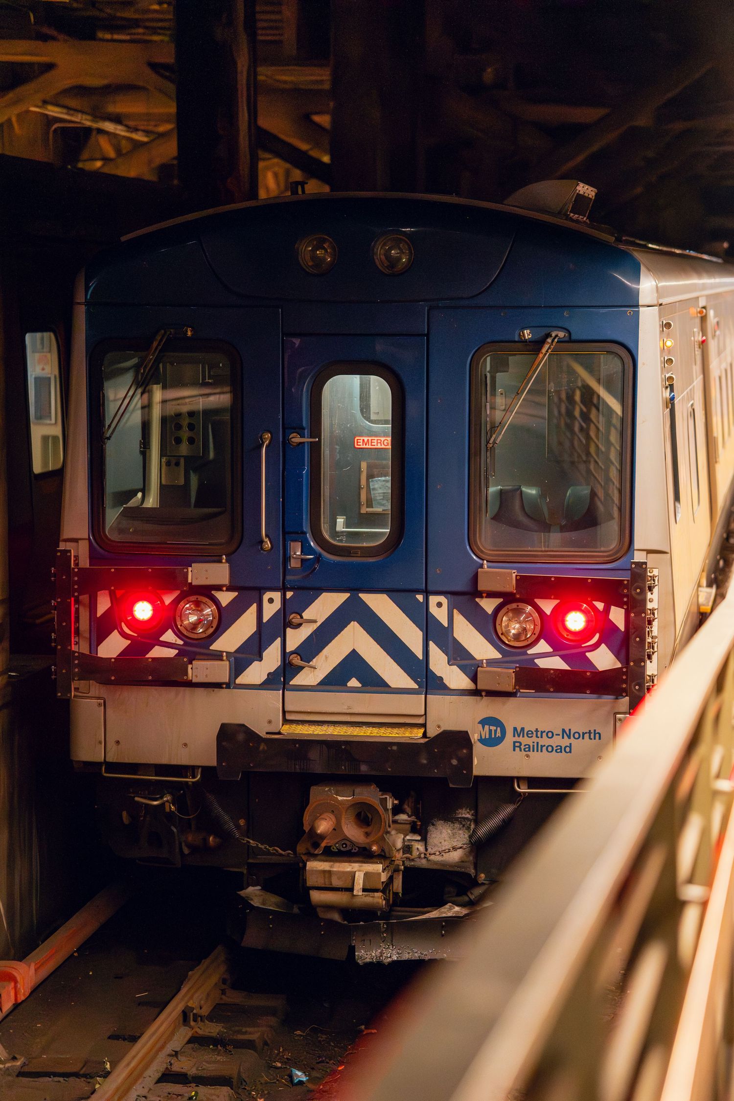 A blue Metro-North Railroad commuter train with red tail lights sits in a dimly lit station.