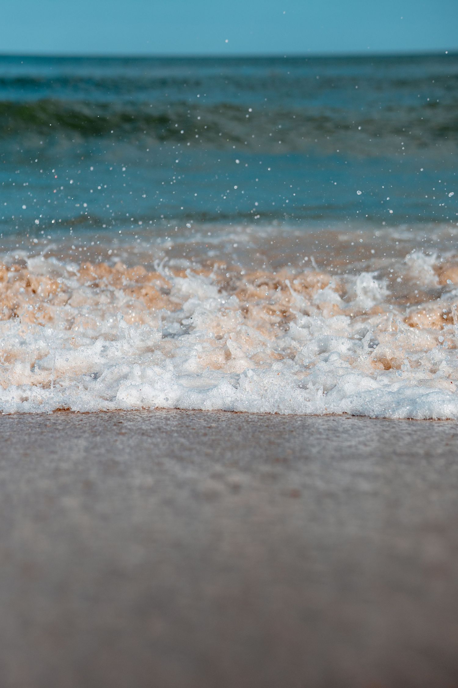 Close-up of frothy ocean waves splashing onto a sandy beach with blue sea in background.