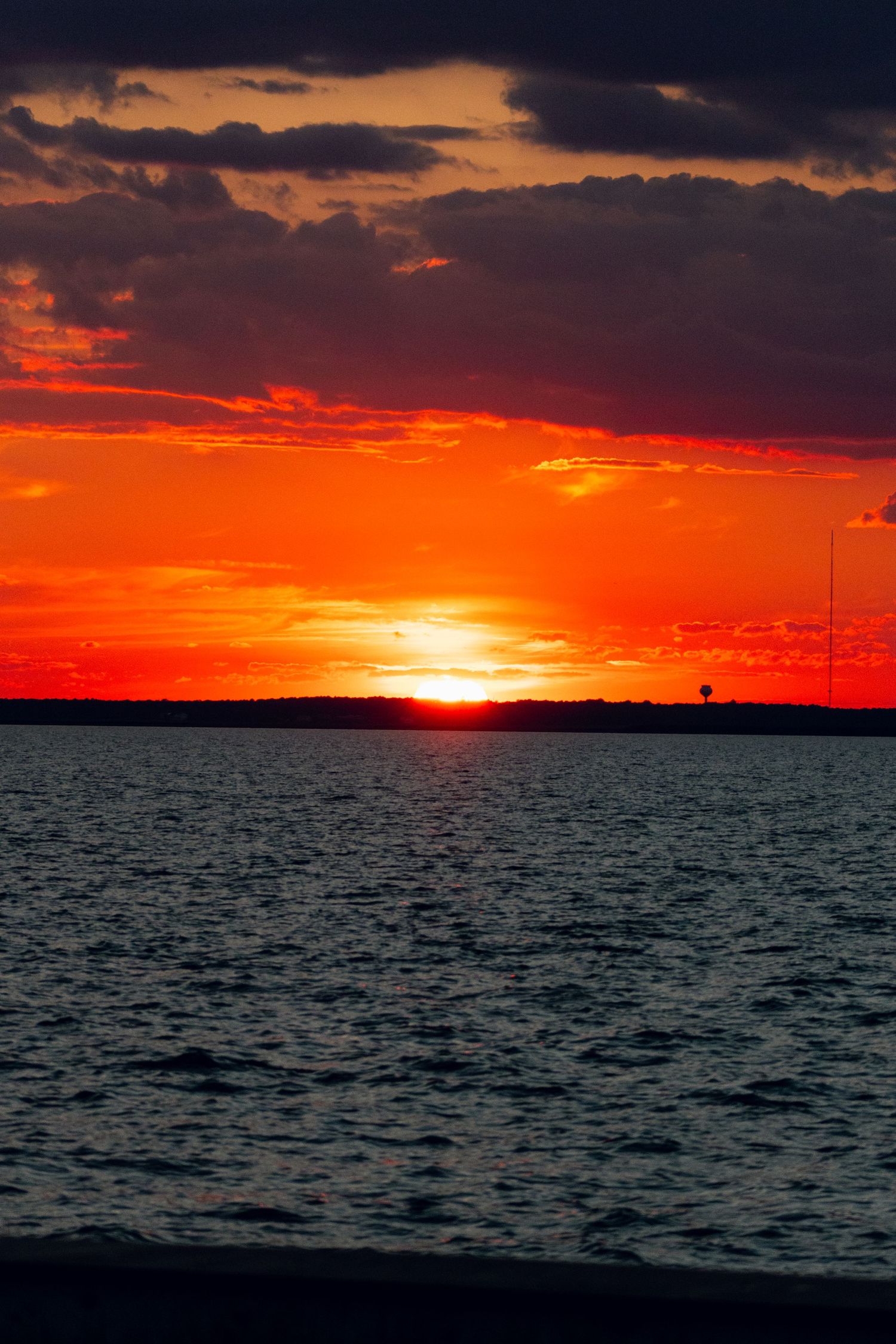 Vertical view of a vivid red sunset over dark water with dramatic cloud formations.