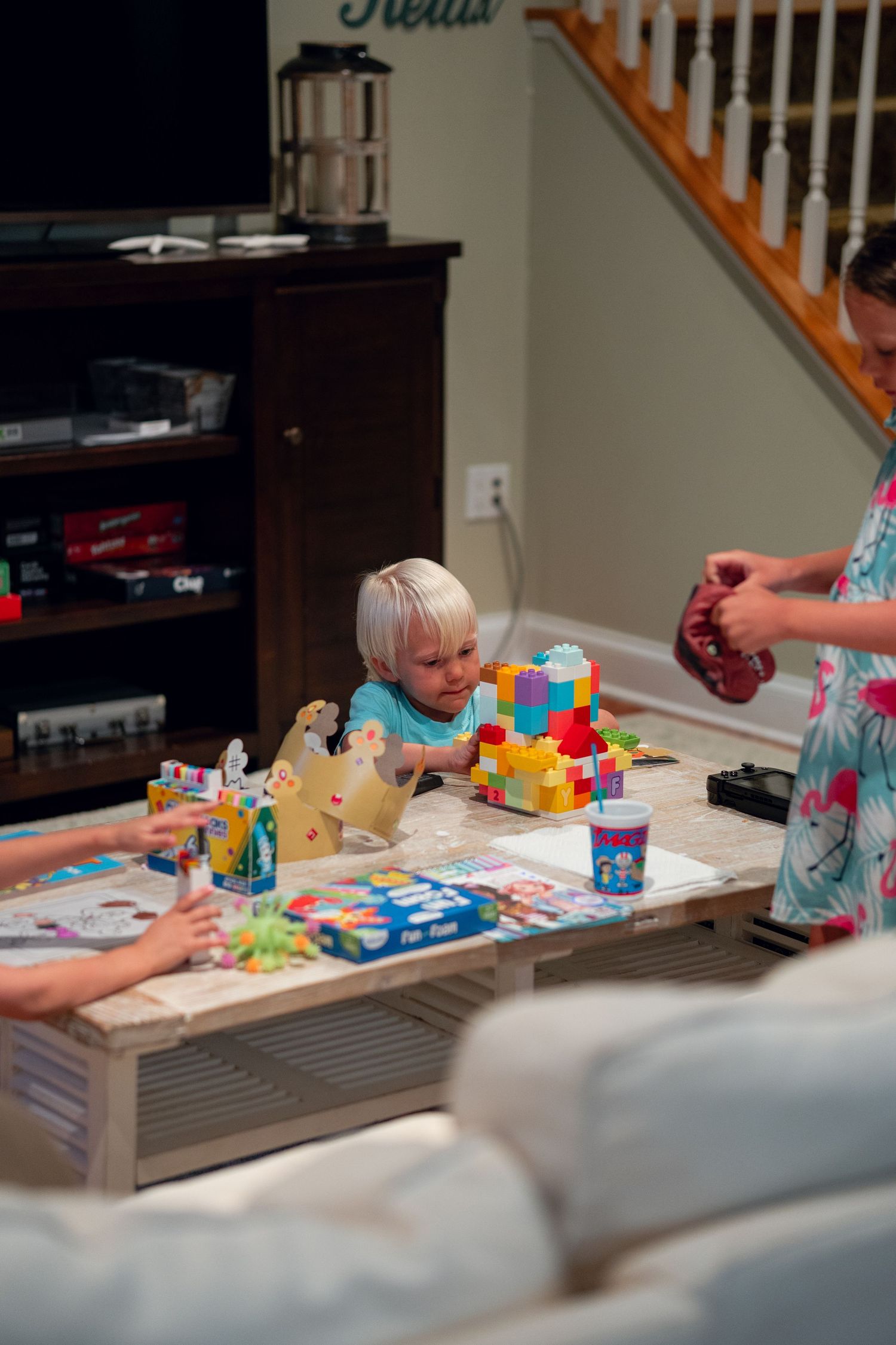 Young blonde toddler playing with colorful stacked building blocks on a coffee table at home.