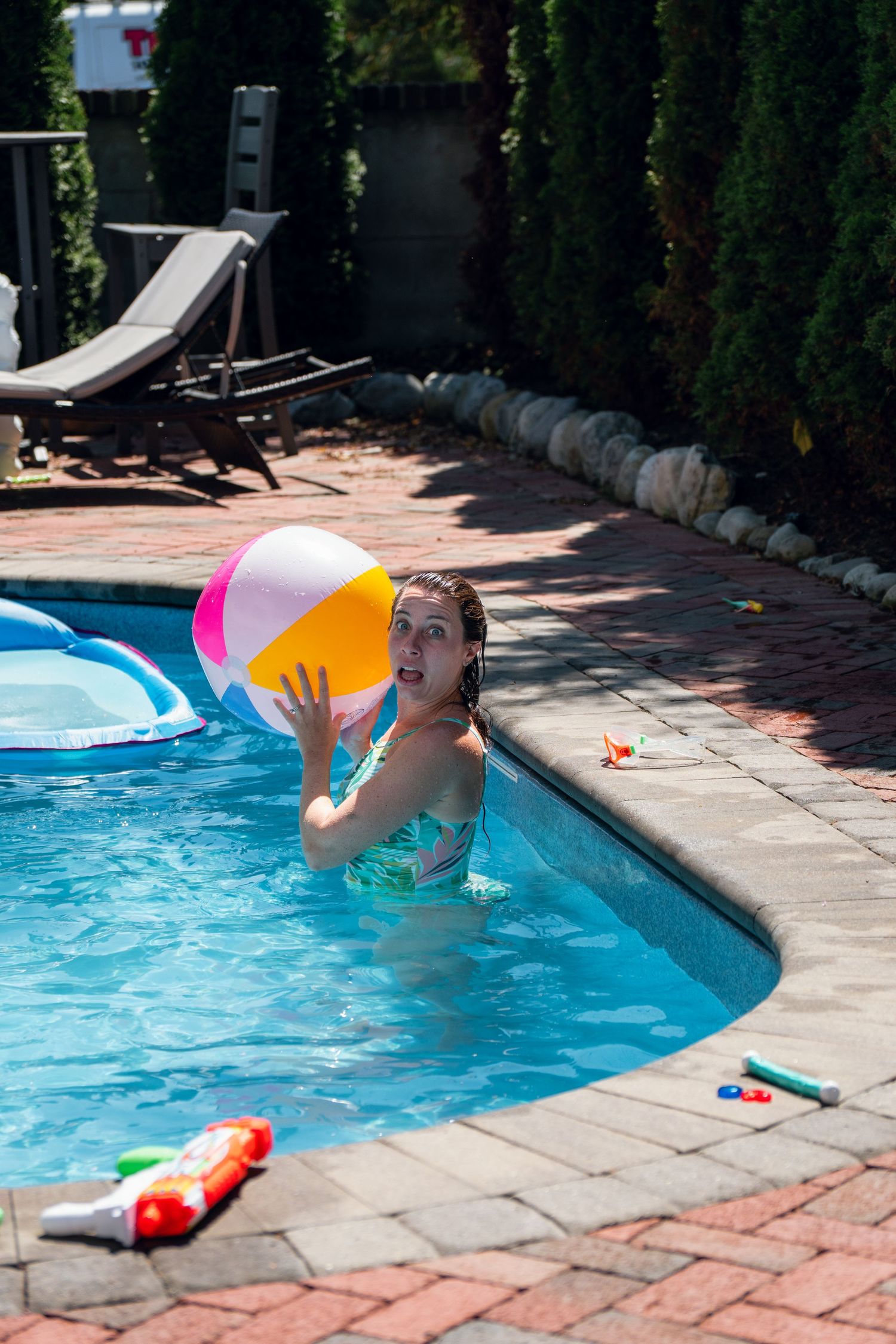 Young girl in swimsuit tossing a colorful beach ball in a backyard swimming pool.