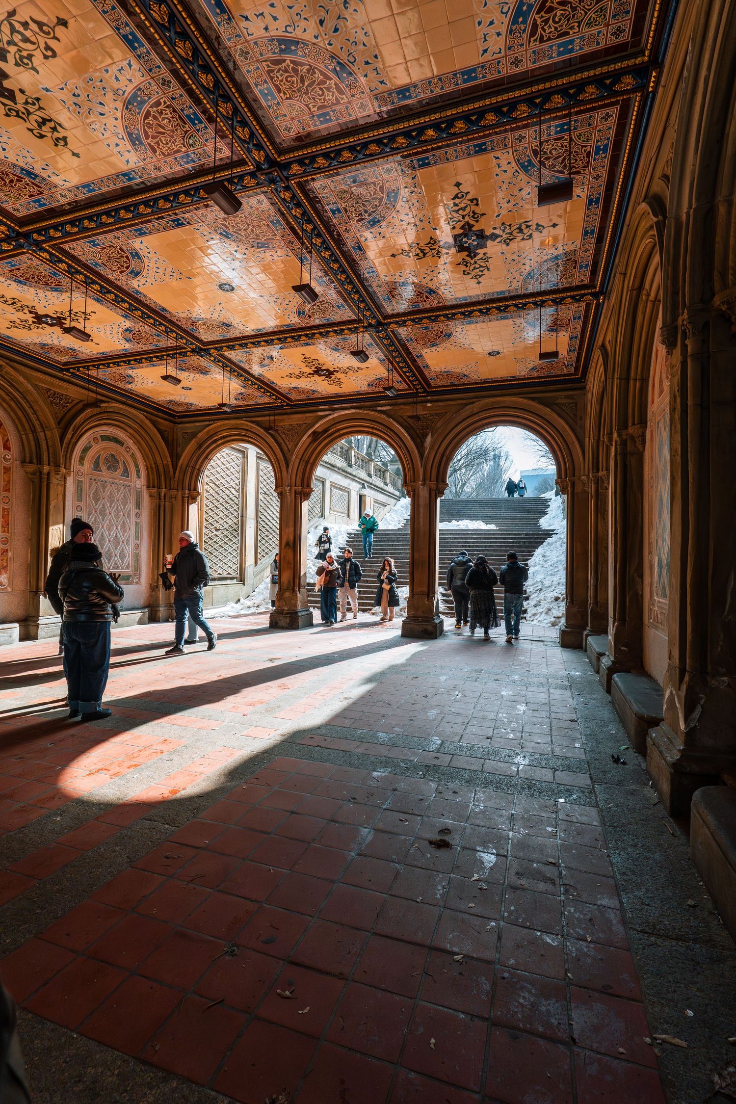 Visitors walk through Bethesda Terrace underpass with decorative tiled ceiling in Central Park, NYC.