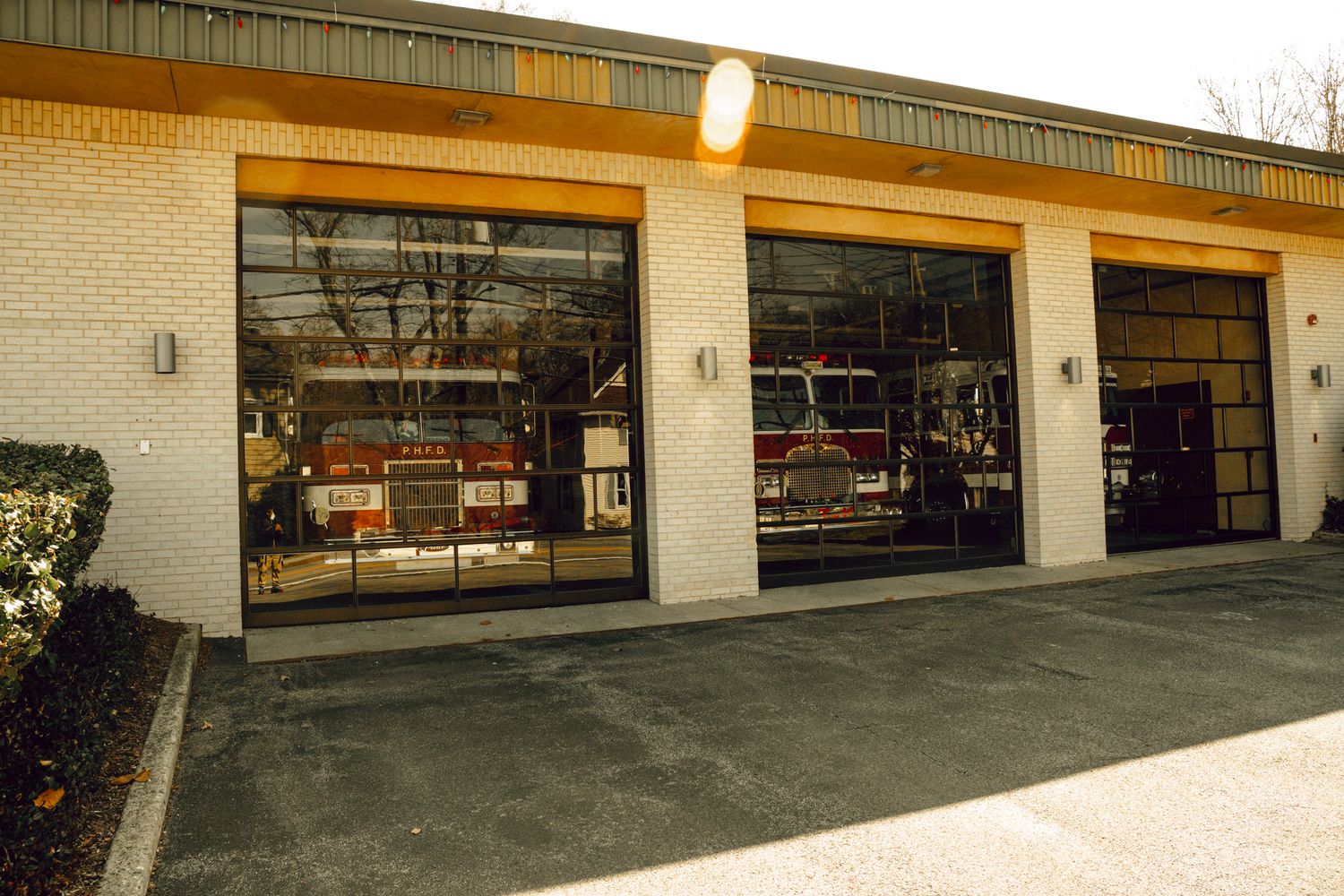 Firehouse exterior with three large glass garage doors housing red fire trucks inside.