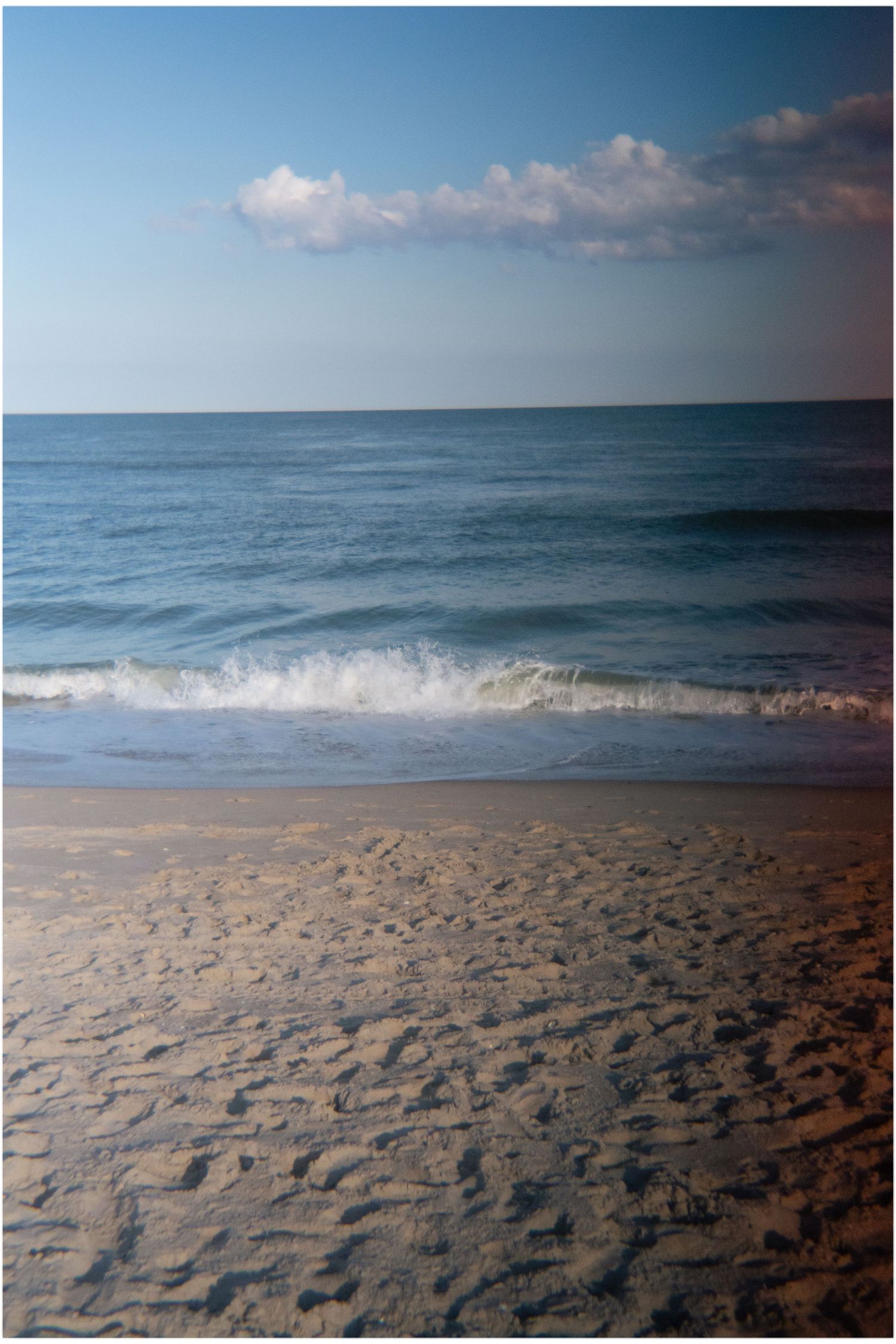 Serene beach scene with turquoise ocean waves, golden sand, and fluffy clouds in a blue sky.