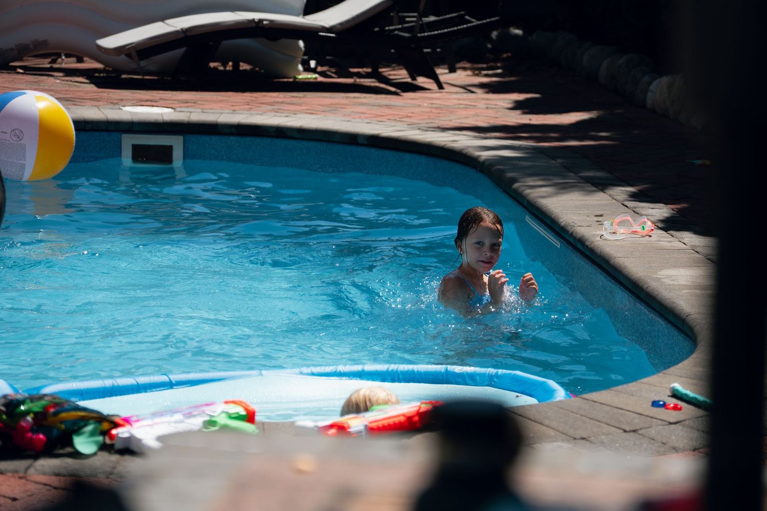 Child swimming and playing in a clear blue backyard pool on a bright sunny day.