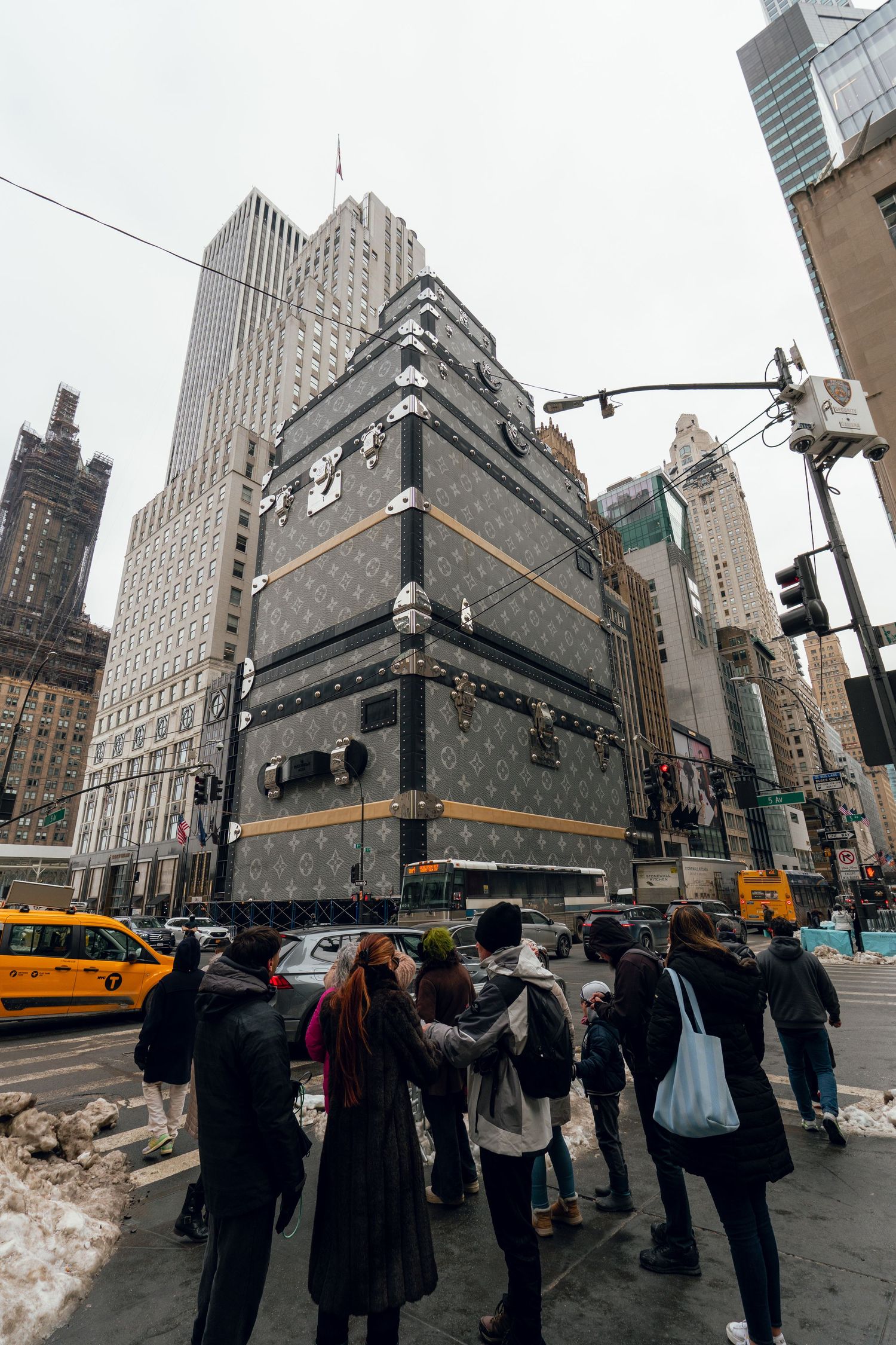 Crowd viewing giant Louis Vuitton trunk-shaped building facade on NYC Fifth Avenue.