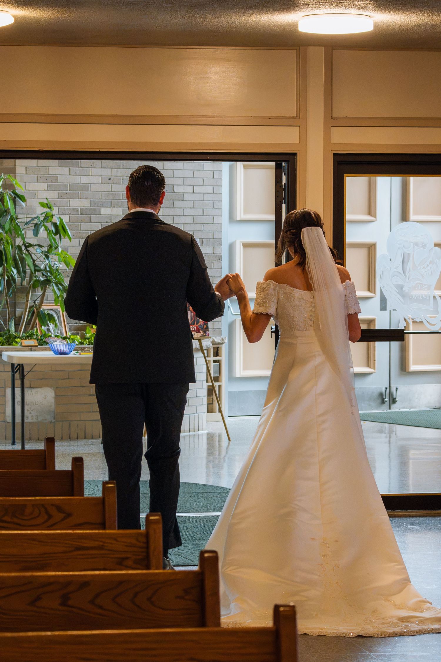 Bride and groom walking hand in hand down church aisle after wedding ceremony, bride in white off-shoulder gown with veil.