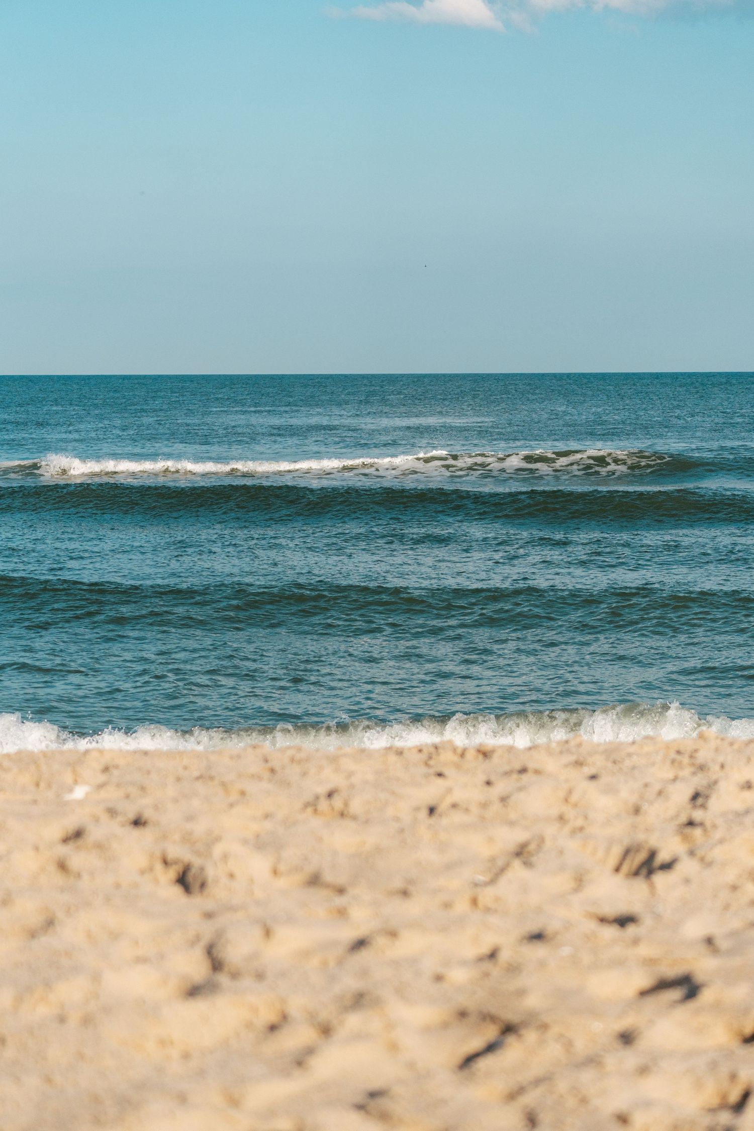 A serene sandy beach with gentle ocean waves rolling in under a clear blue sky.