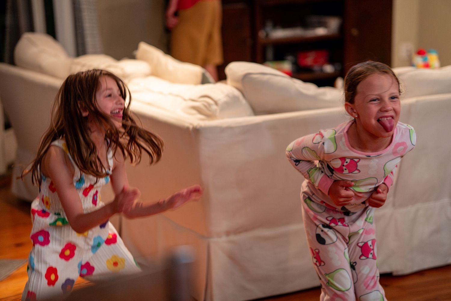 Two girls in pajamas laugh and dance energetically together in a living room.