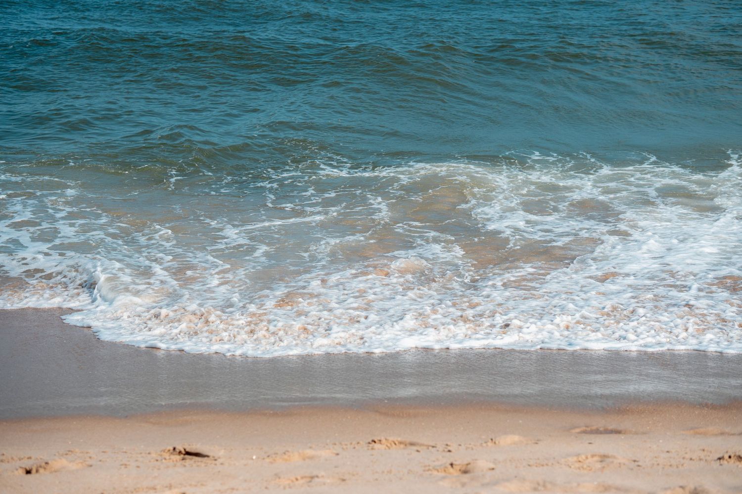 Turquoise ocean waves with white foam gently rolling onto a sandy beach shore.