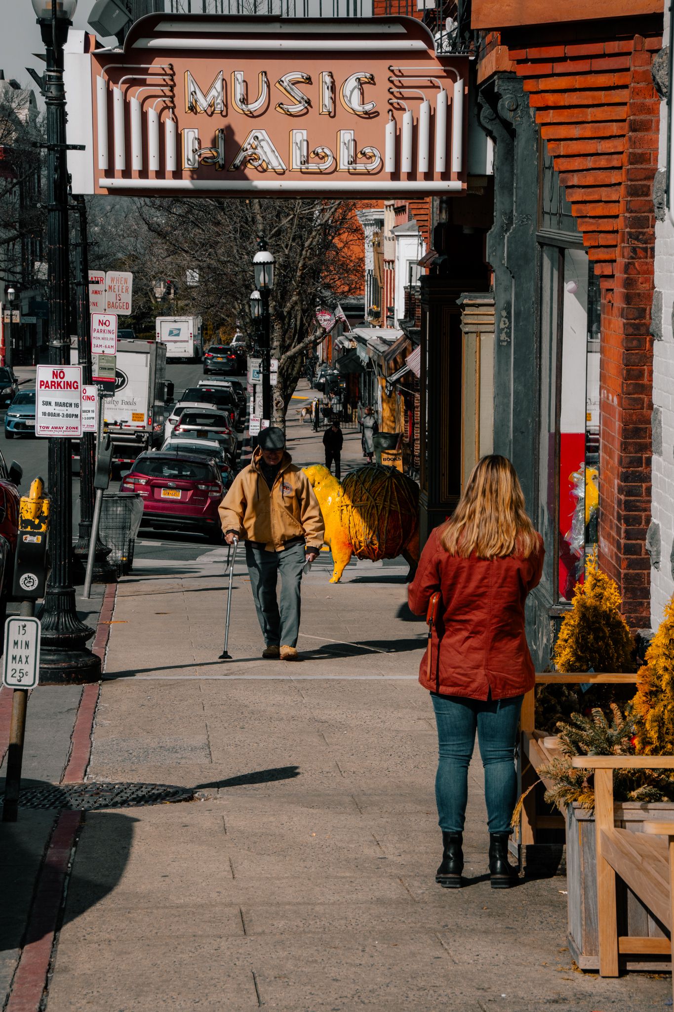 Pedestrians walking under a Music Hall sign on a bustling small-town street.