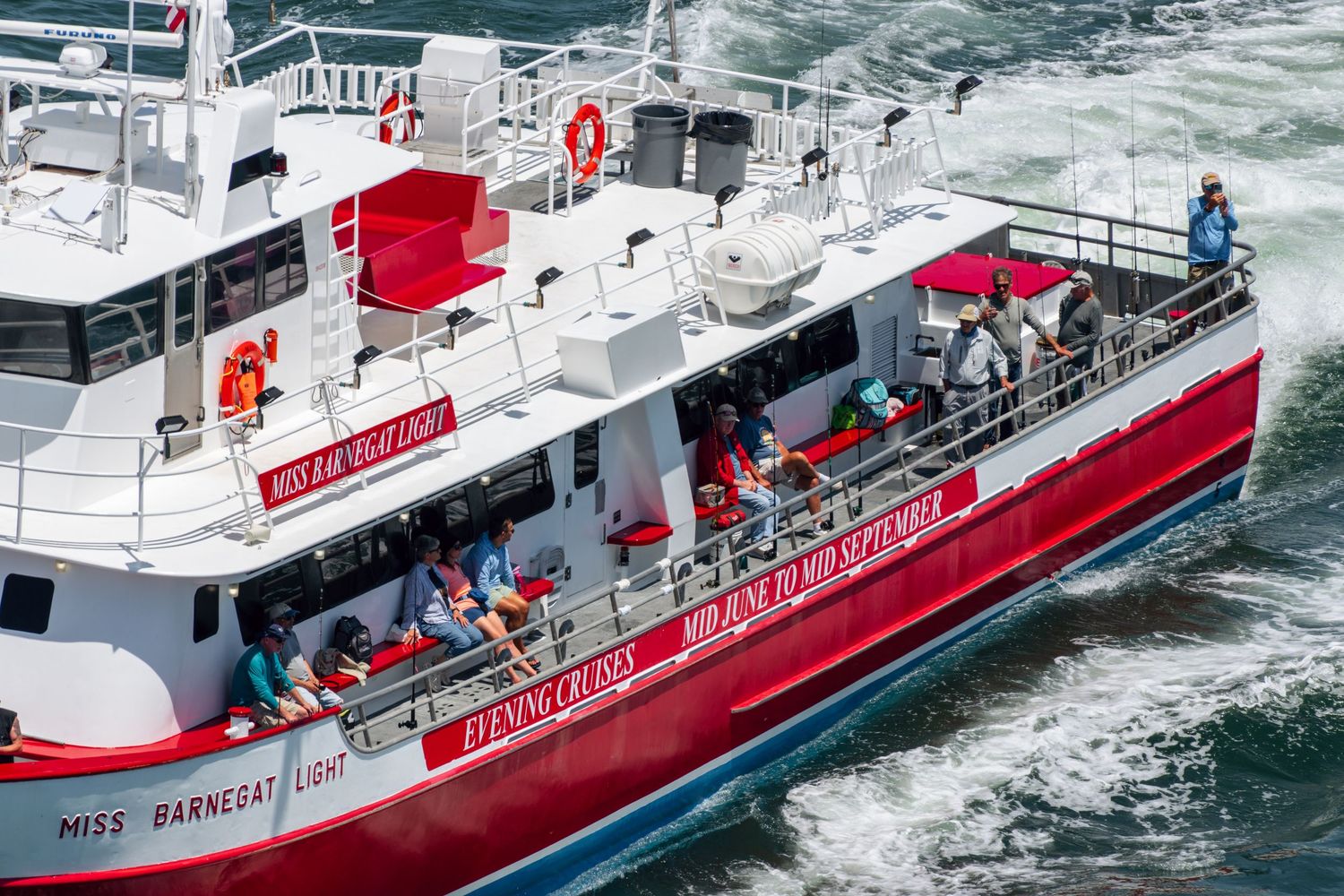Red and white Miss Barnegat Light tour boat with passengers on deck cruising through choppy waters.