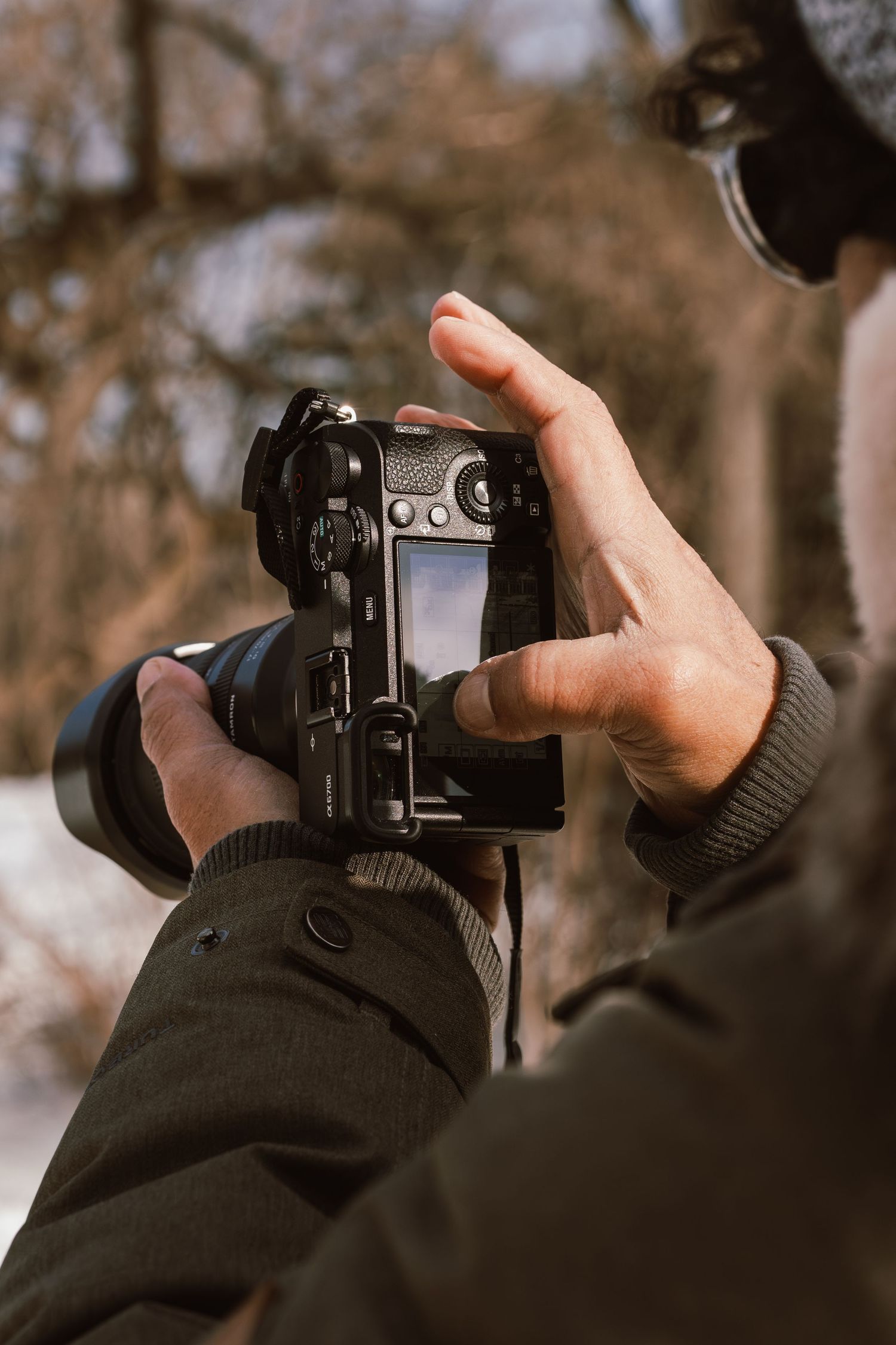 Photographer holding a DSLR camera with articulating LCD screen outdoors in winter, reviewing photos in a snowy park.