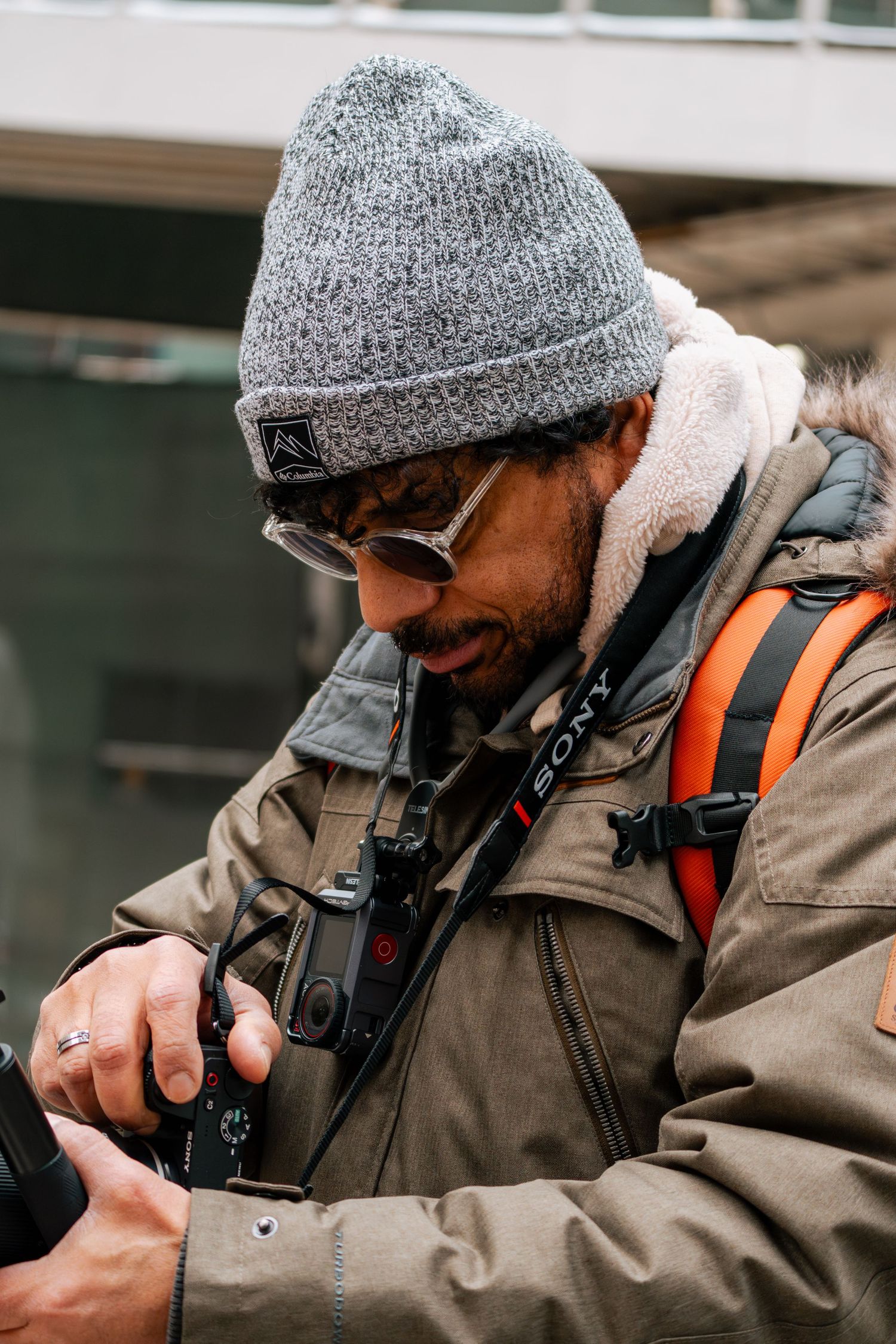 Male photographer in gray beanie reviewing Sony camera settings outdoors in winter.