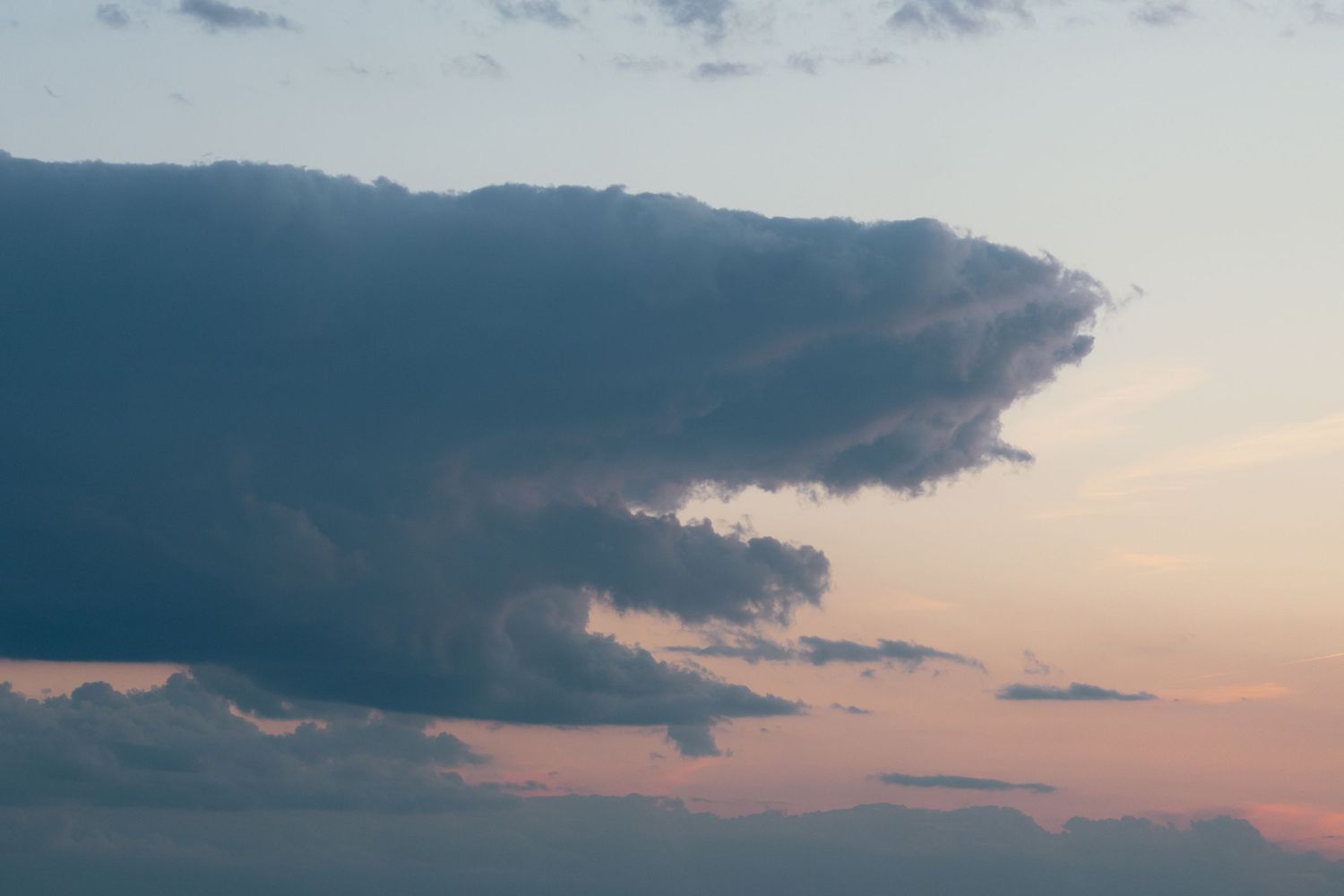 A dramatic large dark storm cloud formation against a soft pink and blue twilight sky.