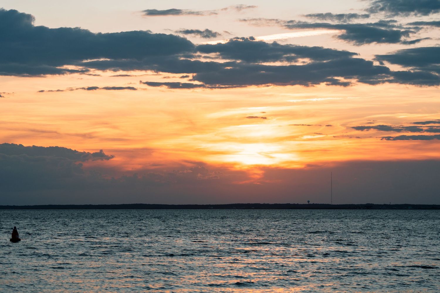 A stunning orange and golden sunset over the ocean with dramatic clouds reflecting on calm water.