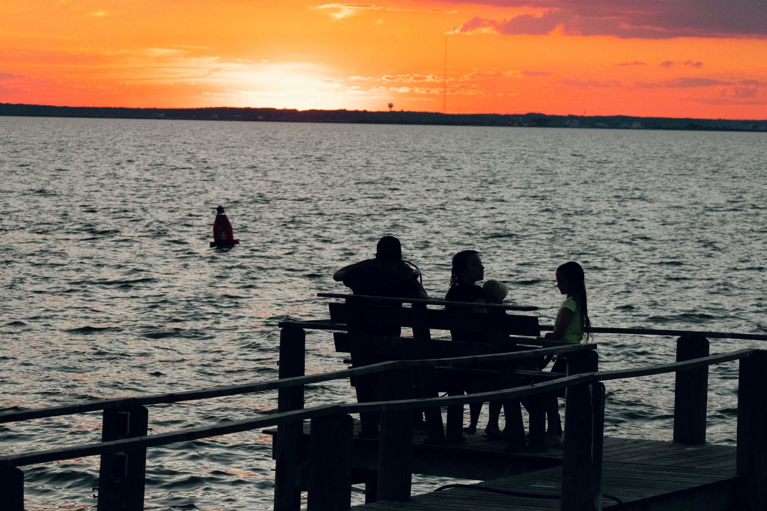 Silhouetted group of people on a pier watching a vibrant orange sunset over water.