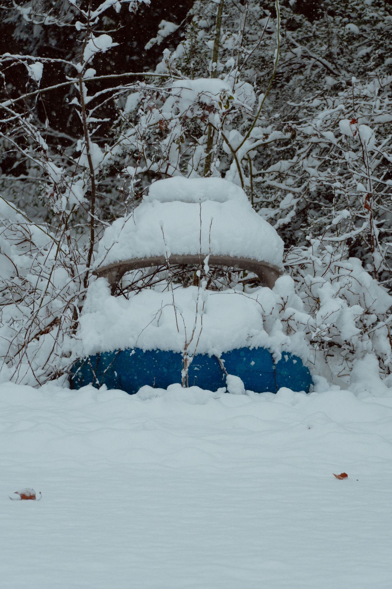 A blue bird feeder buried under heavy snow in a winter garden.