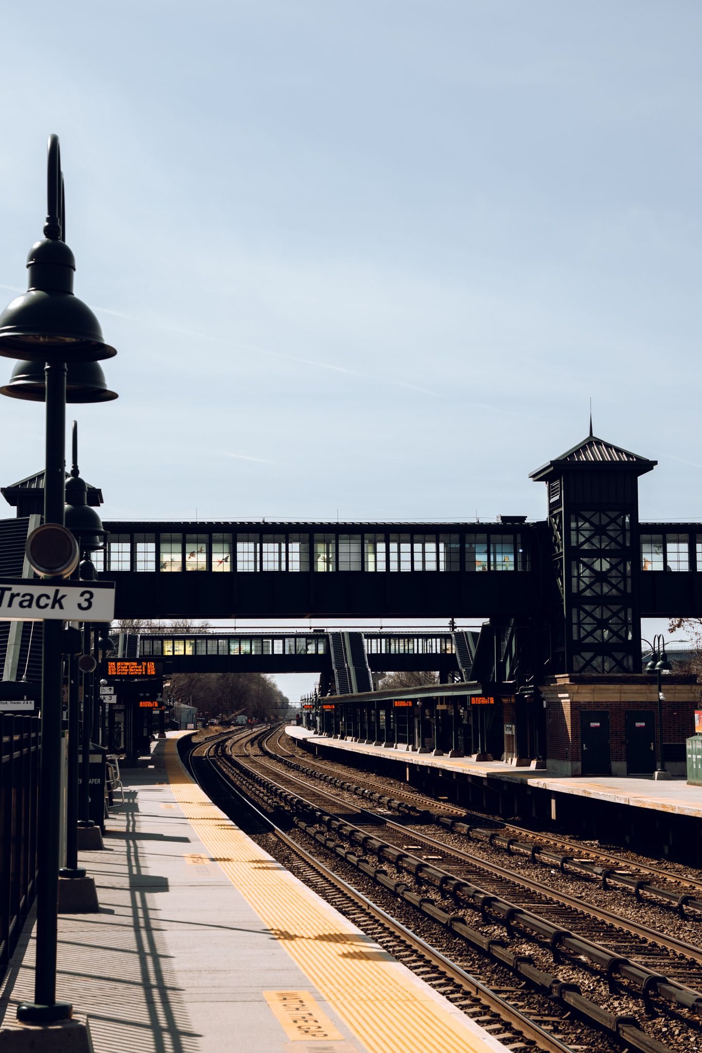 Empty train station platform with curved tracks, overhead bridge, and Track 3 sign.