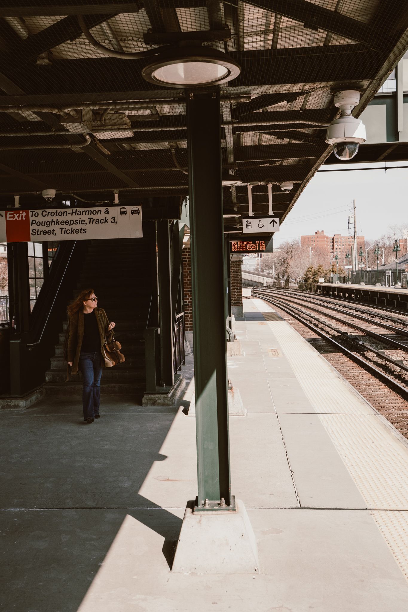 Woman walking on a Metro-North train station platform with signs for Croton-Harmon and Poughkeepsie tracks.