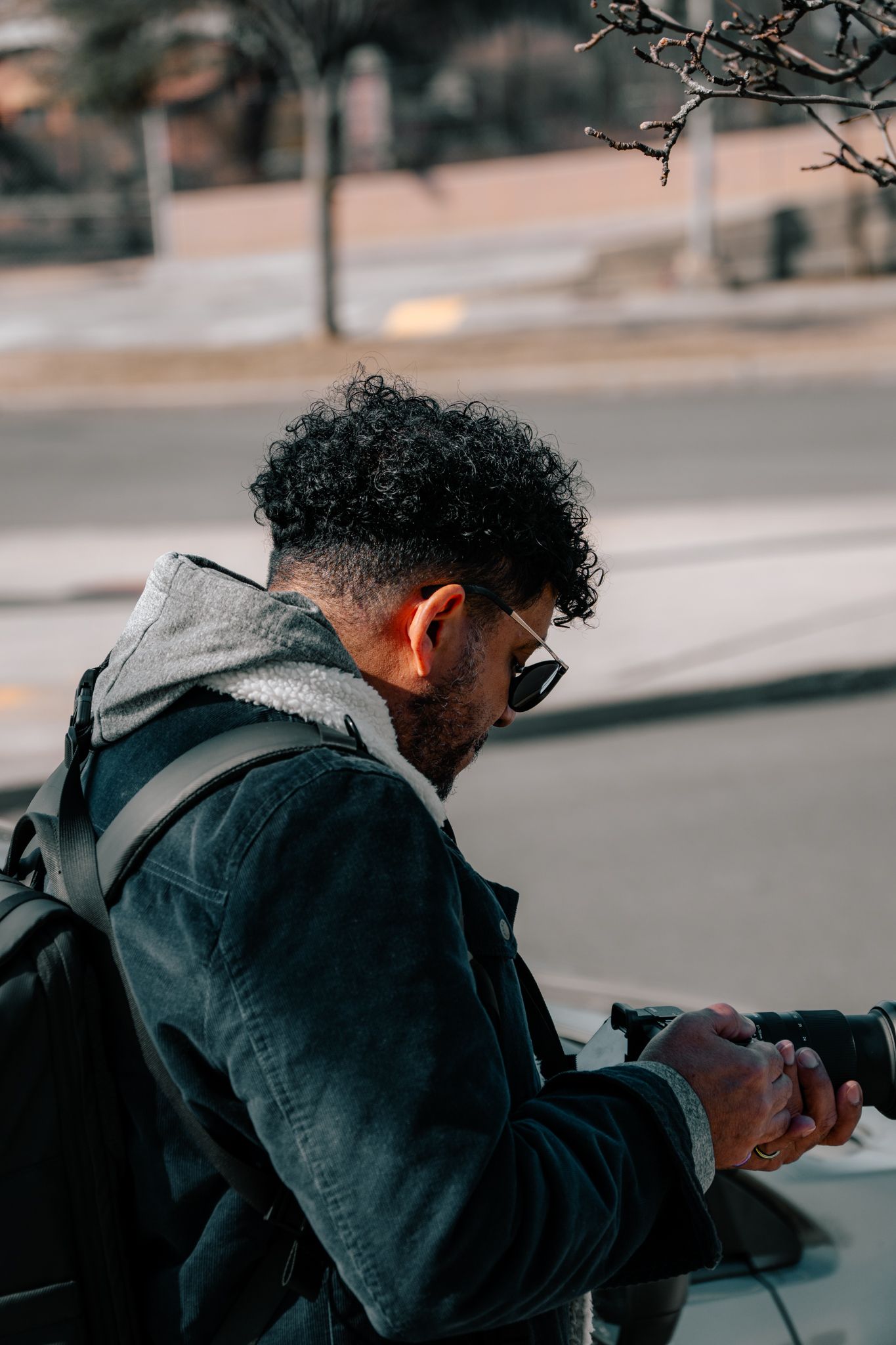 Close-up side profile of a curly-haired man with sunglasses reviewing images on a camera outdoors.