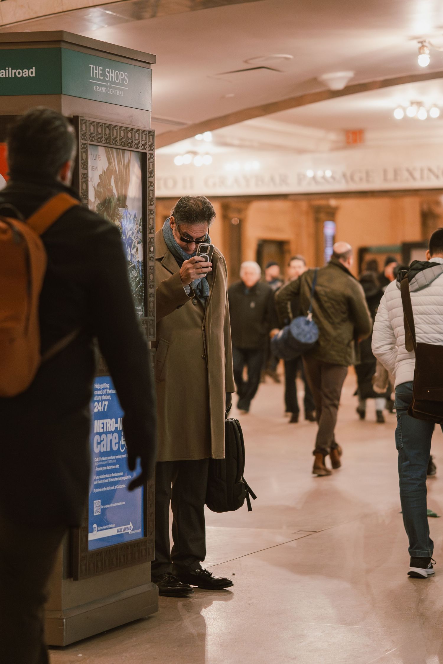 Man in olive coat photographing inside Grand Central Terminal New York.
