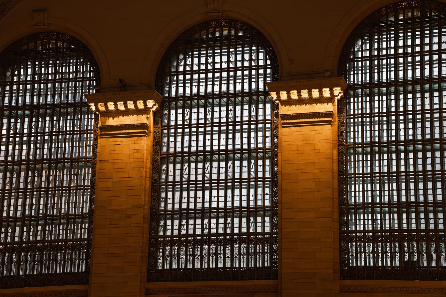 Ornate arched windows with decorative ironwork bathed in warm golden light at Grand Central Terminal.