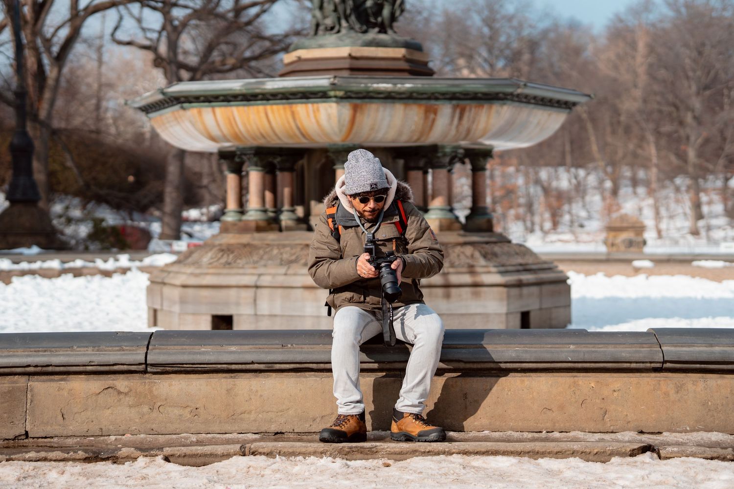 Photographer sitting at Bethesda Fountain reviewing images on camera in snow-covered Central Park.