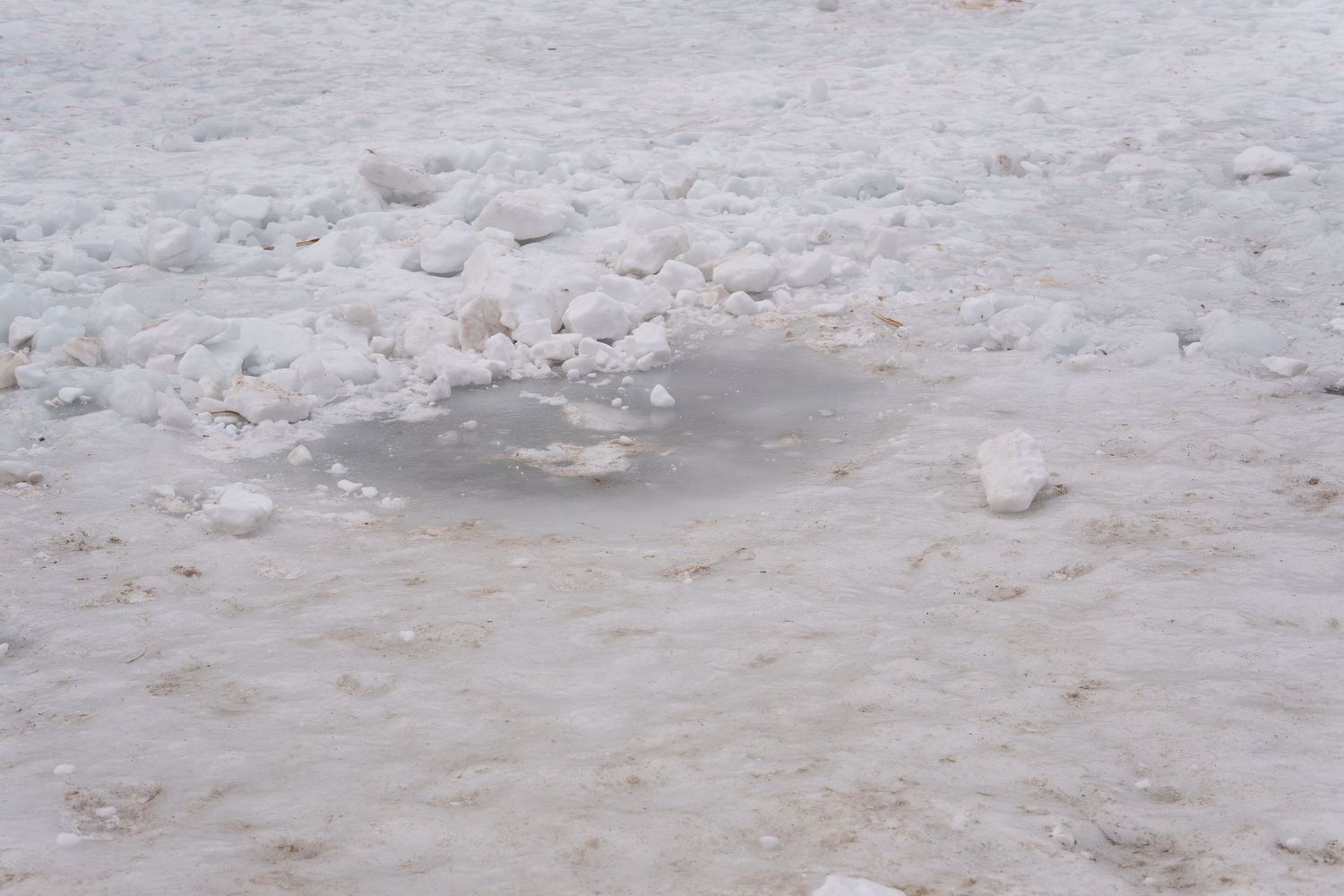 Close-up of cracked and melting ice with snow chunks on a frozen surface.