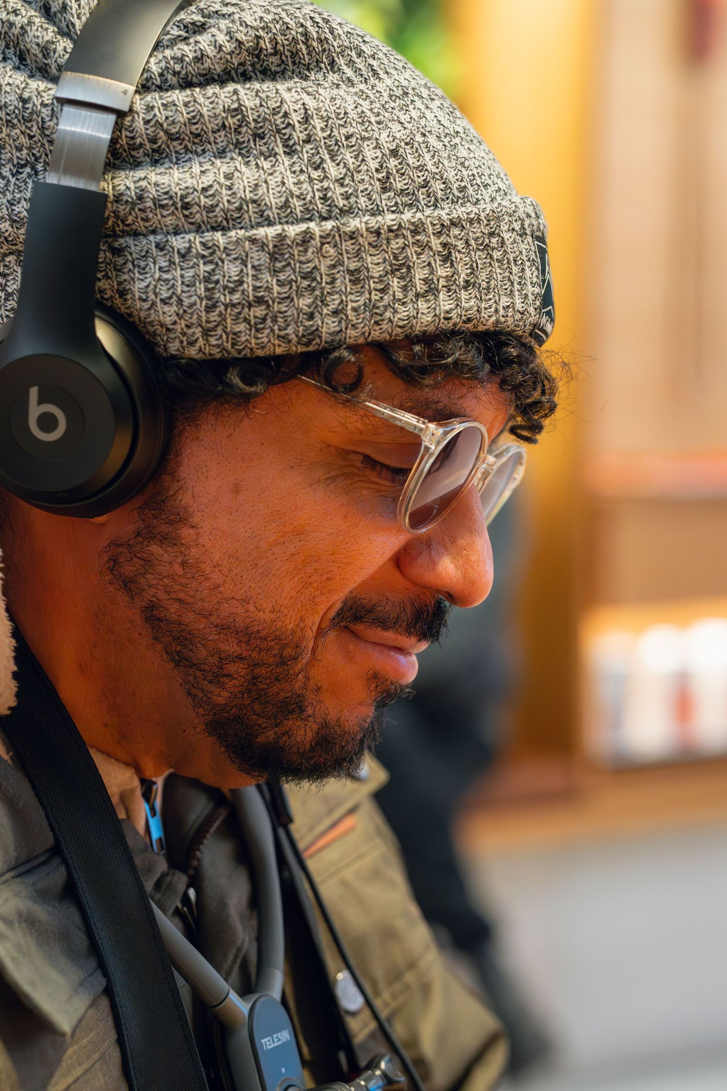 Close-up portrait of a man wearing Beats headphones, gray knit beanie, and round glasses outdoors.