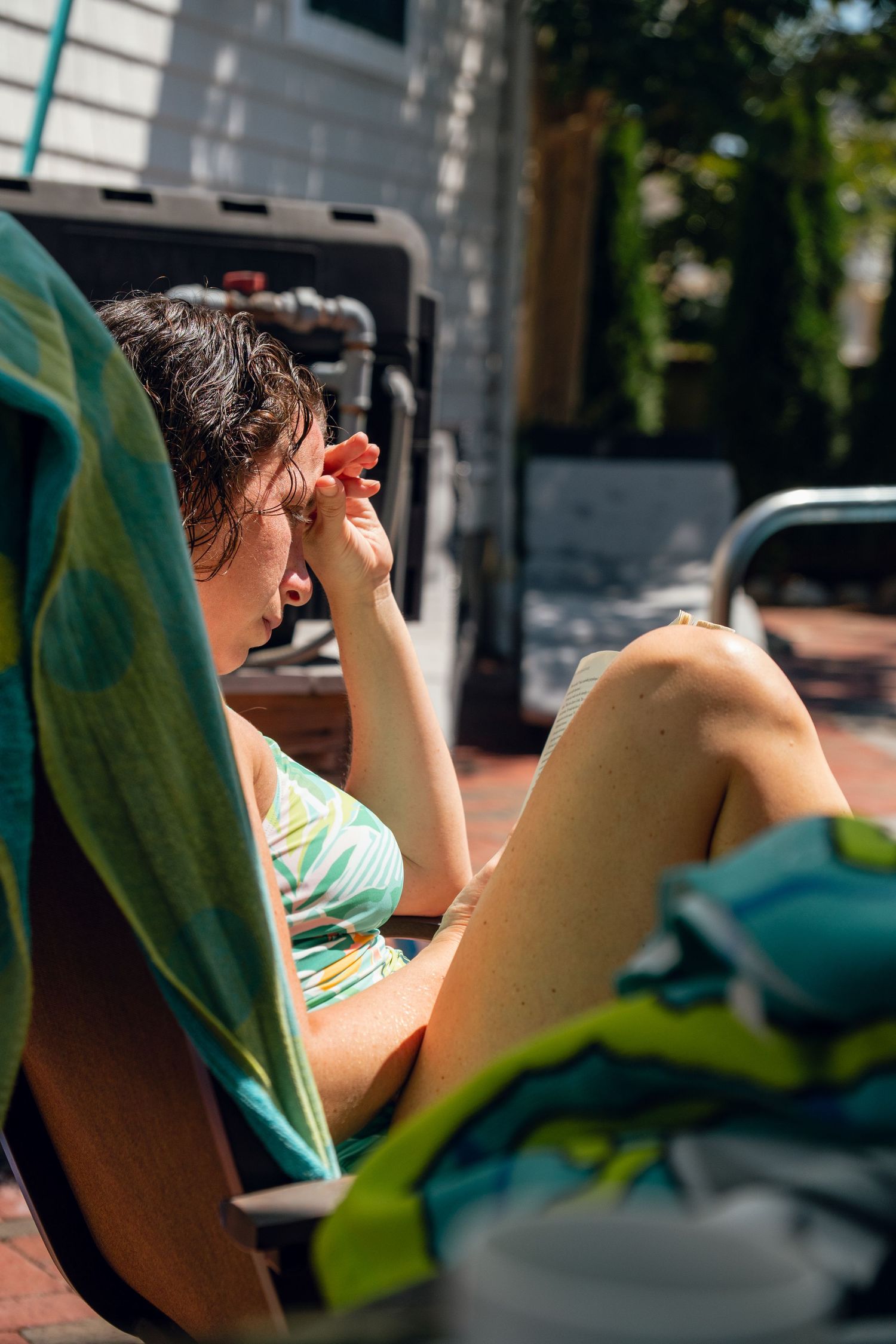 Woman in swimsuit shielding her eyes from the sun while relaxing on a poolside lounge chair.